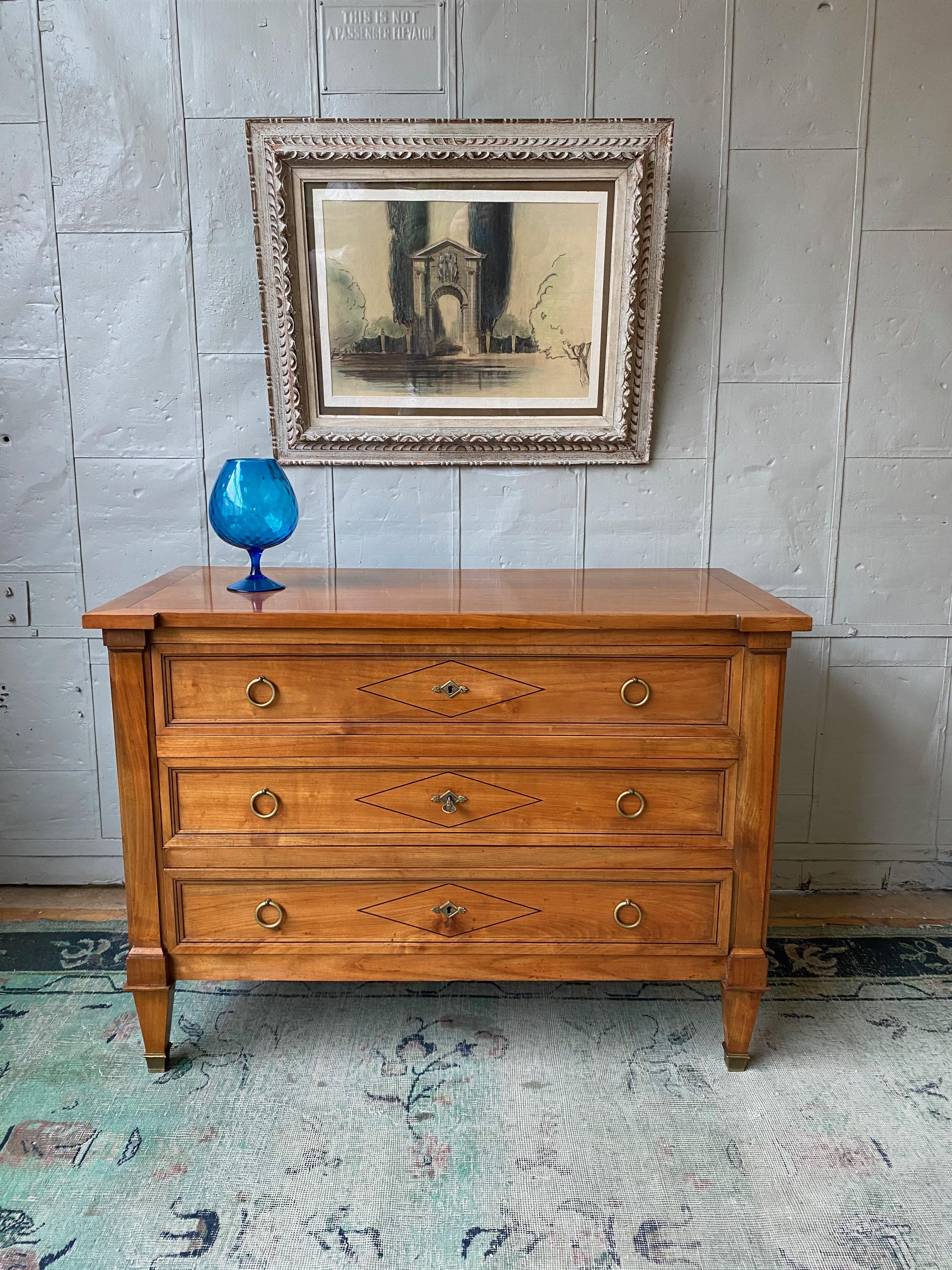 A beautiful three drawer Directoire style French 1940s chest of drawers in light colored fruitwood with contrasting darker wood inlays. In very good vintage condition, it has been recently polished and has the original bronze hardware and sabots. At