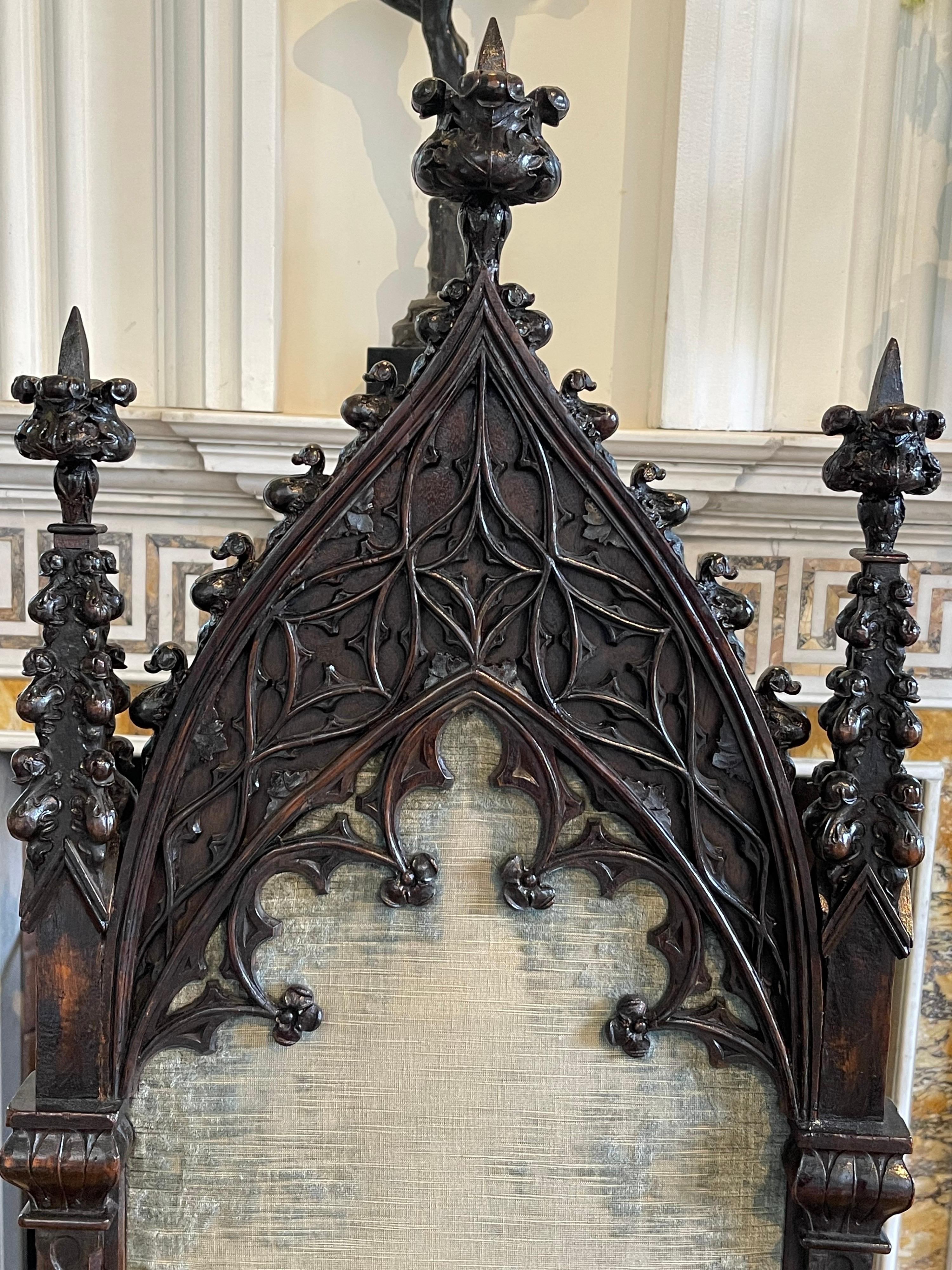 A stunning Gothic style walnut and oak arm chair, hand carved in the late 19th century, when Tudor homes had become popular again. The back looks like a pointed arch window flanked by foliate finials.