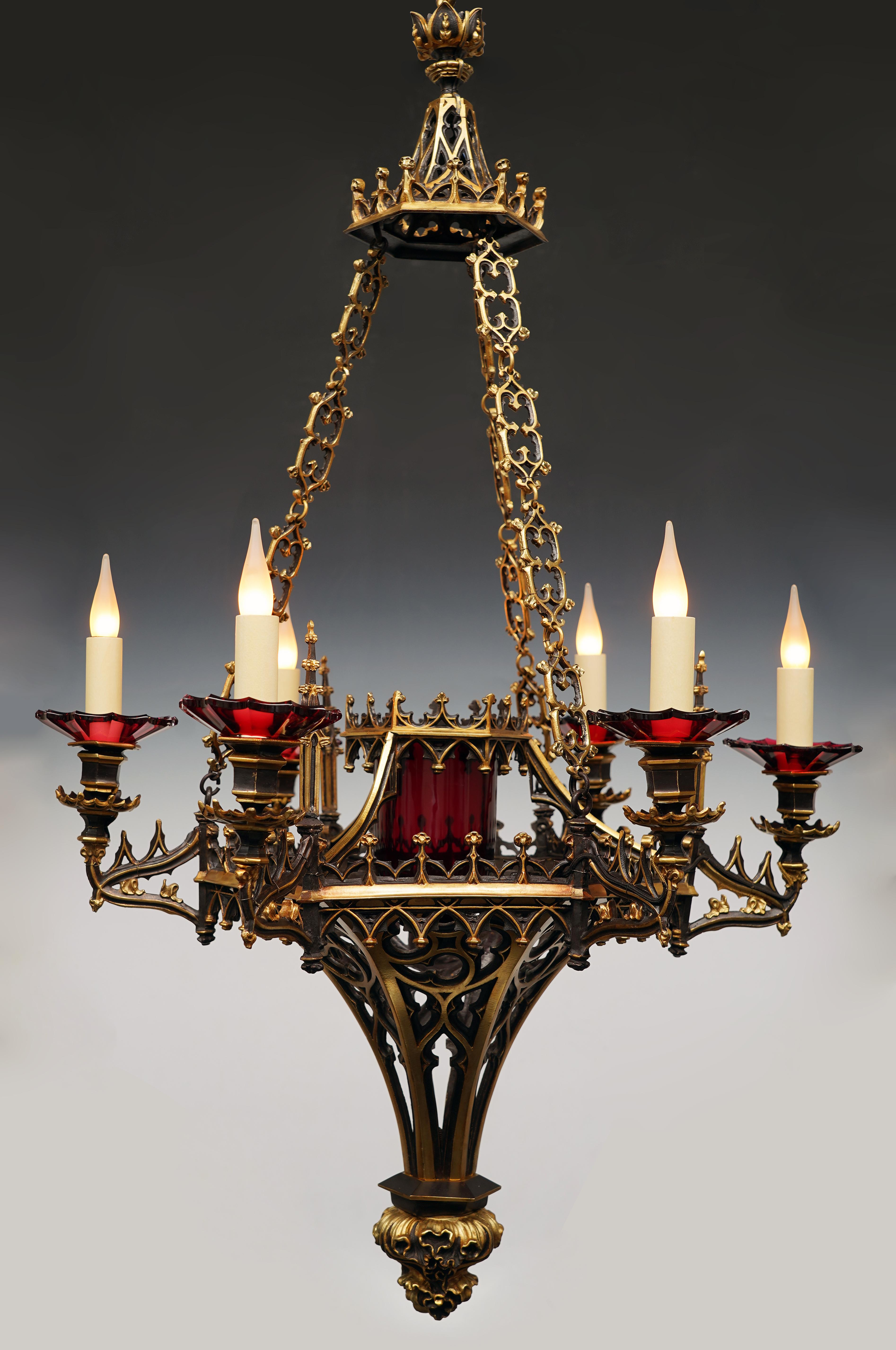 Seltener neugotischer Kronleuchter mit sechs Lichtern aus patinierter Bronze mit goldenen Highlights. Der sechseckige architektonische Schaft, der gotischen Bögen ähnelt, wird von einer rot getönten, gekrönten Verrine zentriert und hat 6 Lichtarme,
