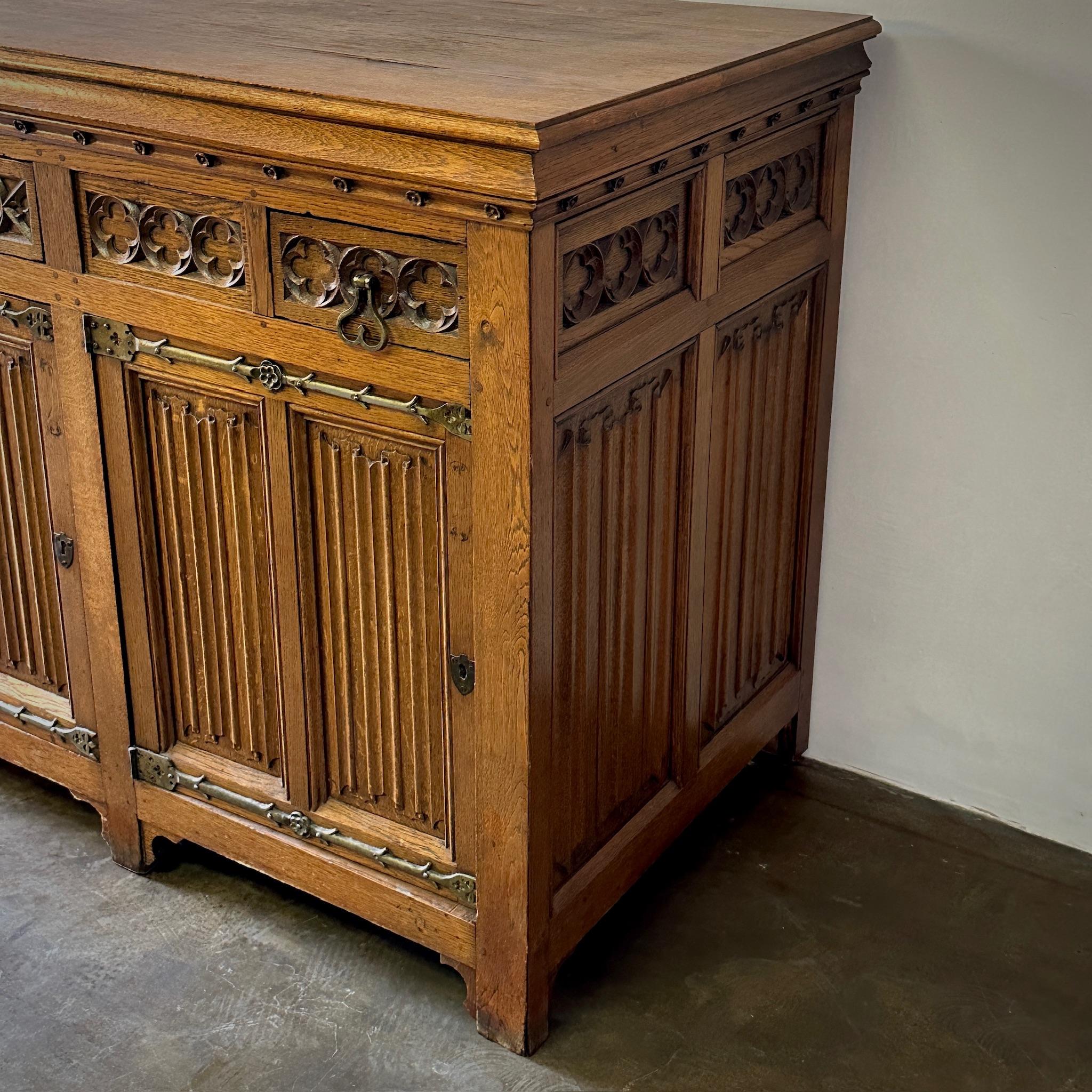 French neo-gothic sideboard in a handsome dark oak. Features beveled cupboards with interior shelving and three carved drawers with wrought iron hardware. A classic 19th century piece with an understated sense of gravitas.

France, circa