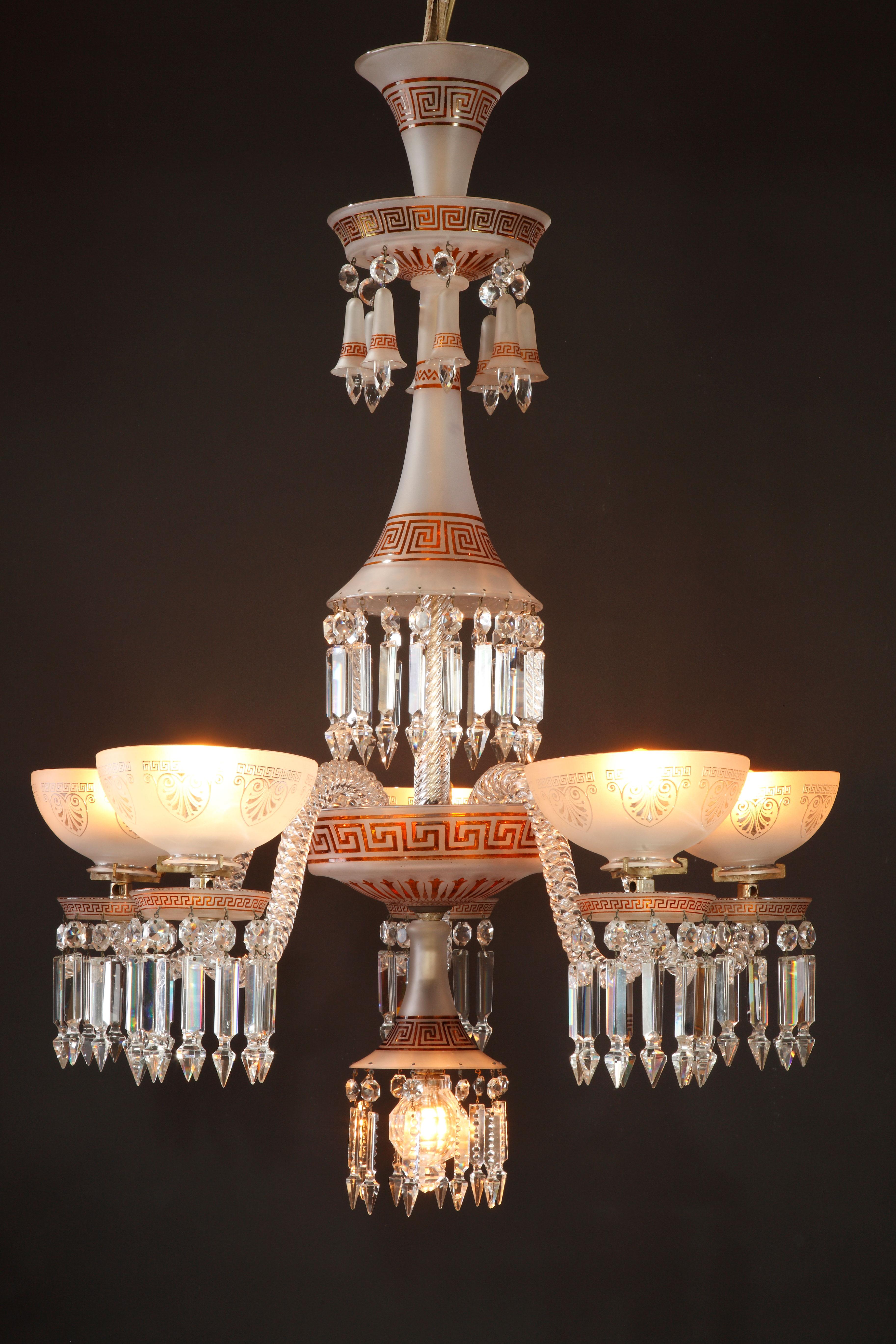 Charming six-light chandelier attributed to Baccarat in clear and opaque cut crystal decorated with Greek friezes in orange tones. The central shaft, formed of inverted cones and cups, ends with a light concealed by a sphere with two crystal sides.