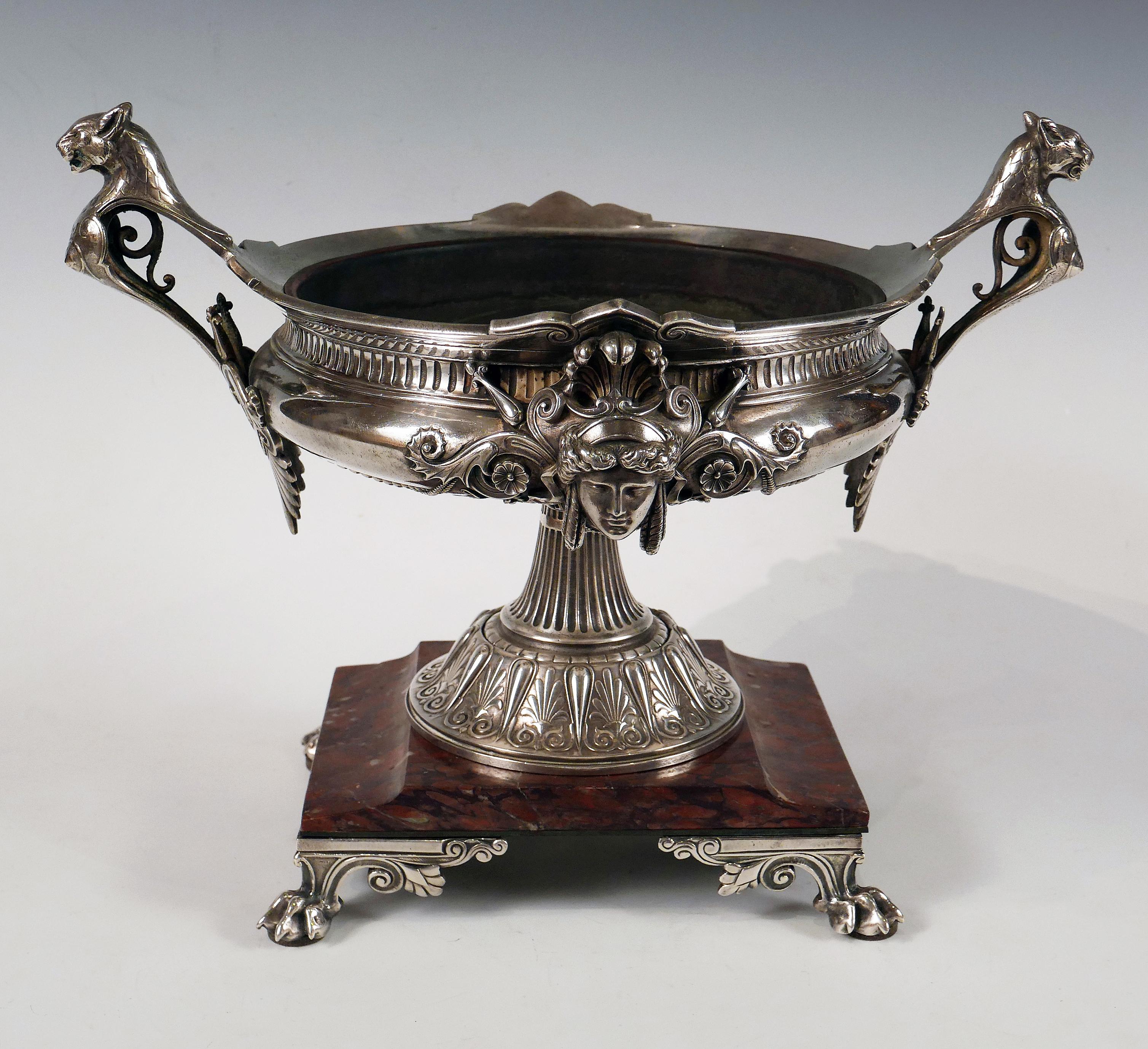 Beautiful silvered bronze neo-Greek style bowl in a circular shape, adorned on the body with female masks in the antique style and on the sides with handles in the shape of busts of lionesses ending in palmettes. The fluted pedestal is surrounded by