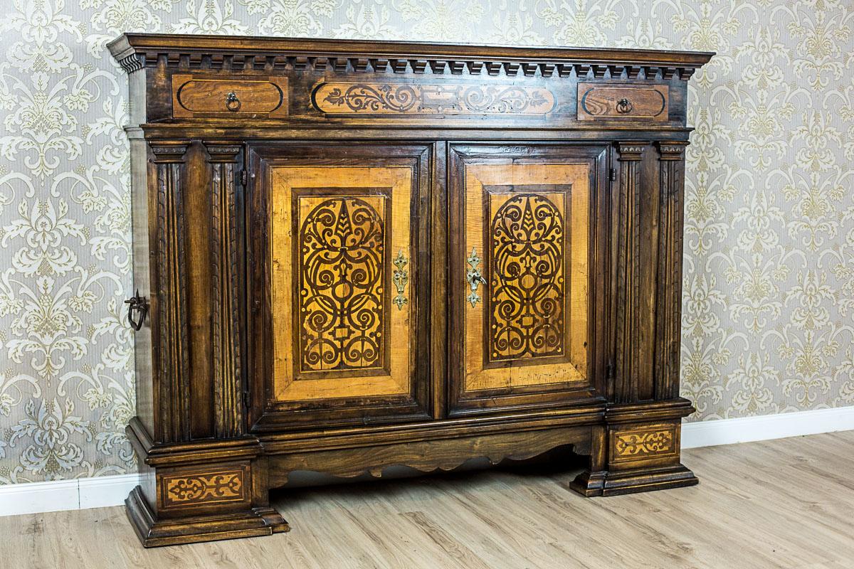 We present you this massive, two-door neo-Renaissance commode made of solid oak wood. The whole is supported on legs that are an extension of its sides, and finished with a profiled socle cornice. The double-leaf doors of the commode are flanked by