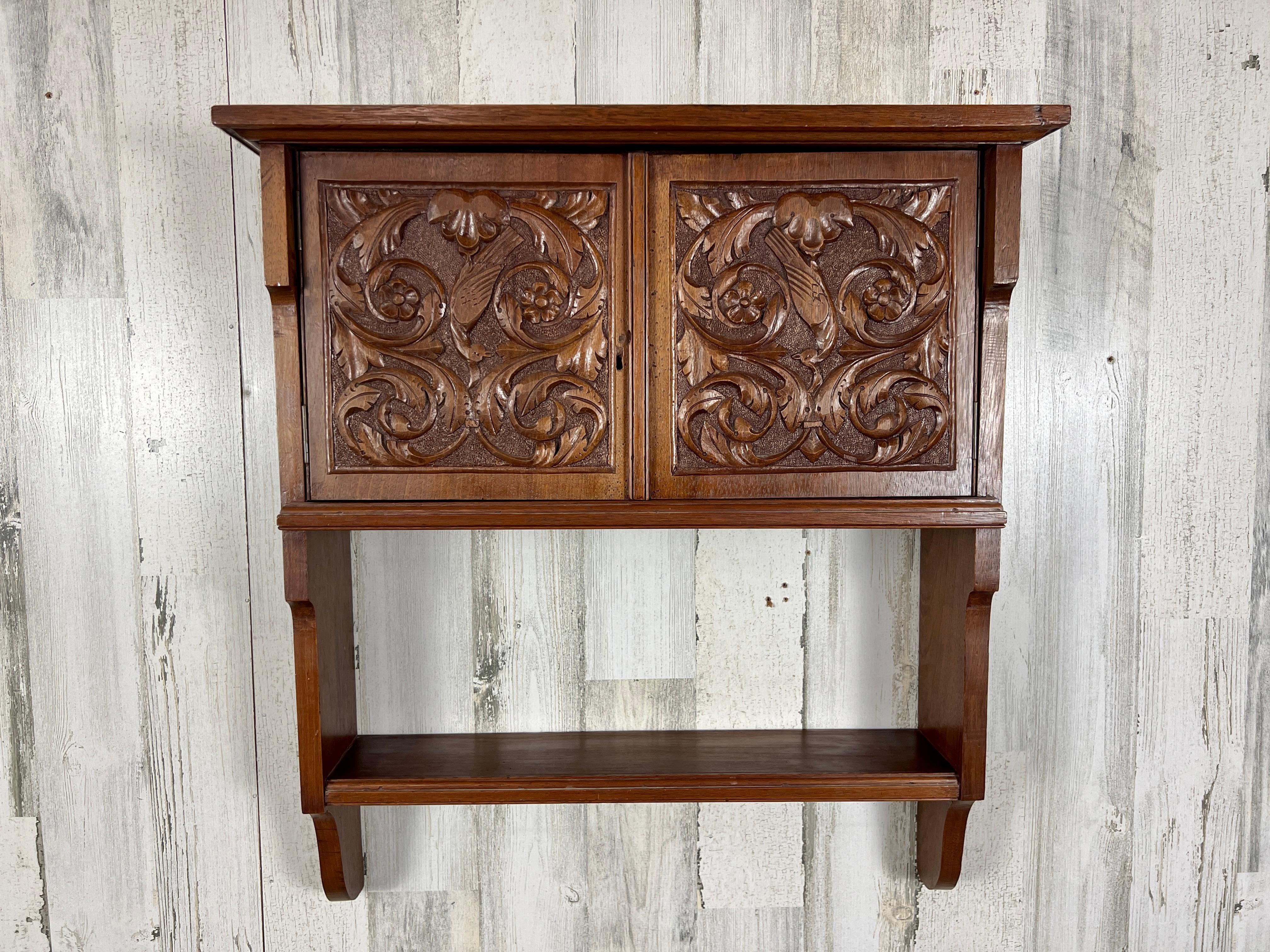 Hand carved solid walnut hanging wall cabinet  with two carved doors and a shelf down below probably made in France or Belgium.  Circa 1920