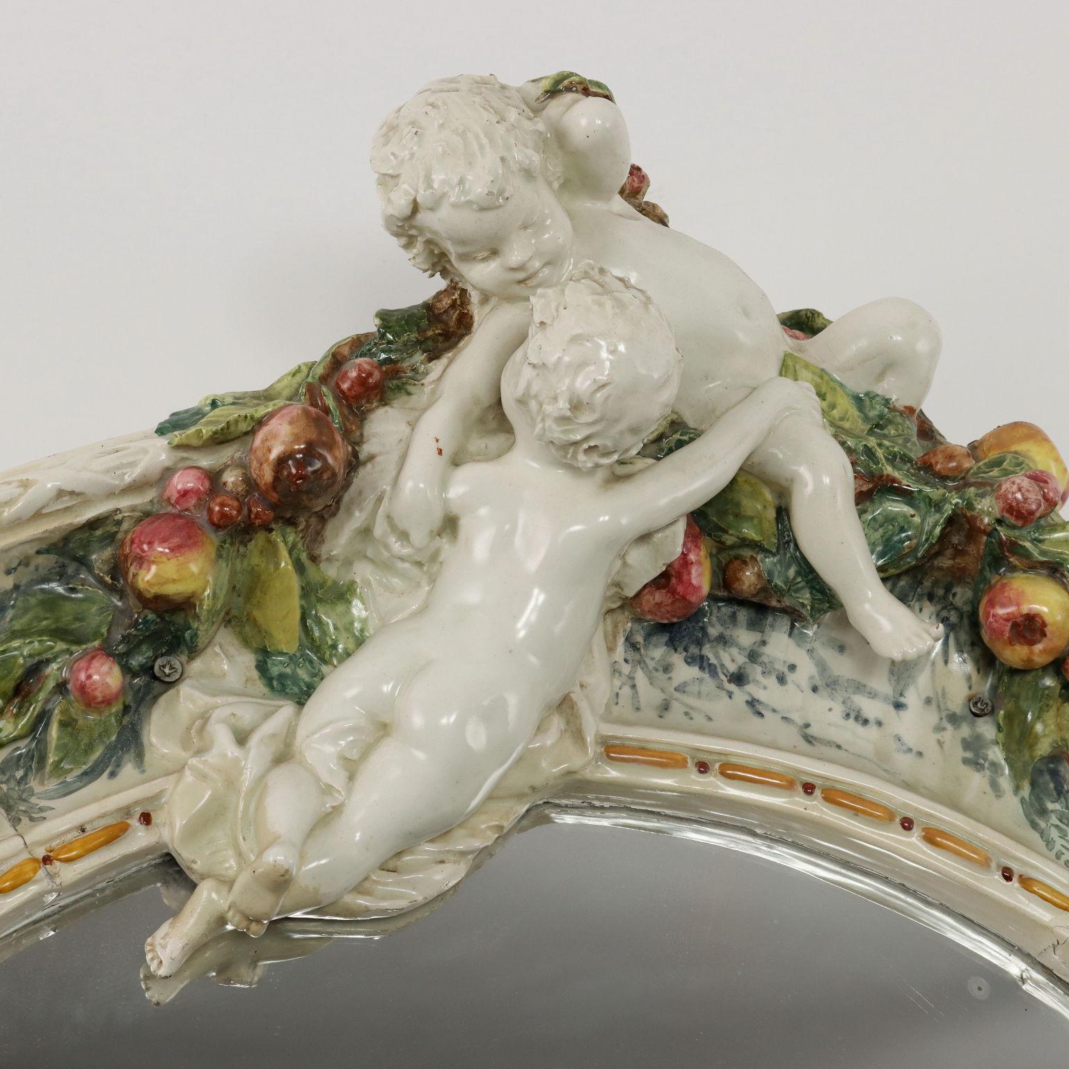 Neo-Renaissance mirror, imitating the painted terracotta of the Florentine Della Robbia workshop. With frame in glazed and glazed terracotta, decorated with festoons of fruit and two cherubs.