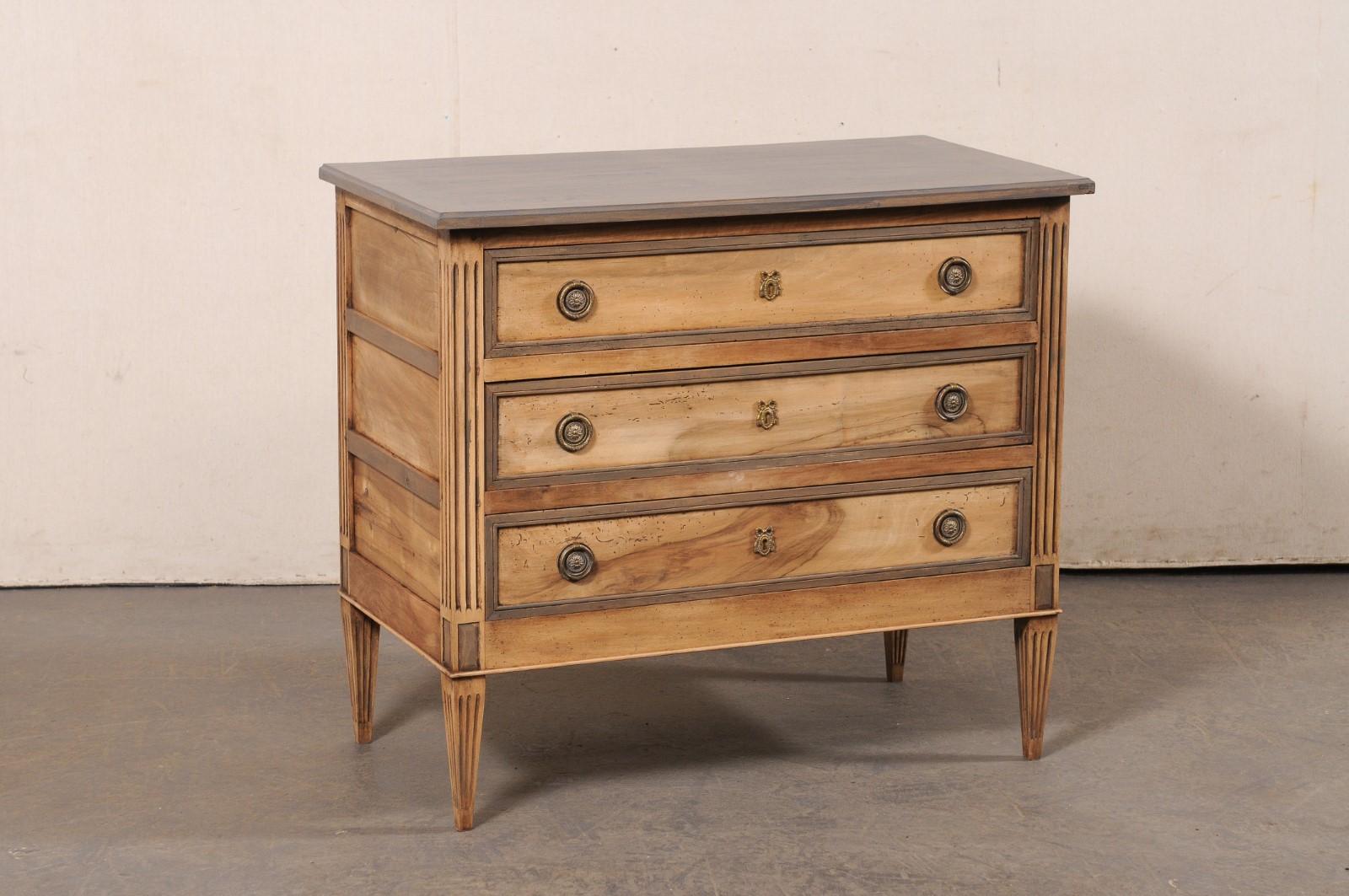 A French Neoclassic carved and painted wood commode from the 19th century. This antique chest from France features a rectangular-shaped top, which slightly overhangs the neoclassical style case that houses three recessed-panel drawers, flanked