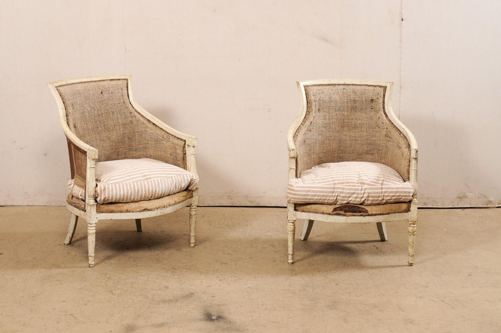 A French Neoclassical pair of carved-wood and upholstered tub-style armchairs from the 19th century. This antique pair of bergères occasional chairs from France have upholstered, tub-style backs with softly curved wooden top rail that slopes down