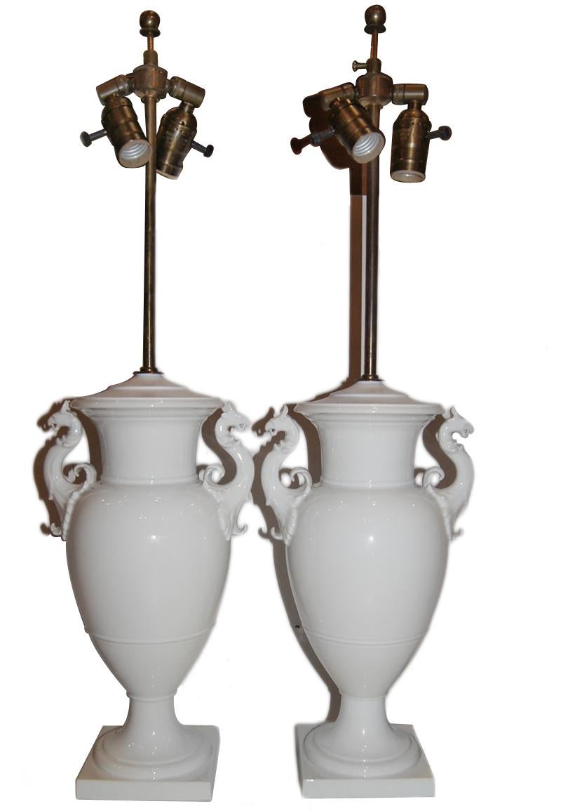Pair of circa 1900's English porcelain table lamps in the shape of urns with griffin handles.

Measurements:
Height of body: 15