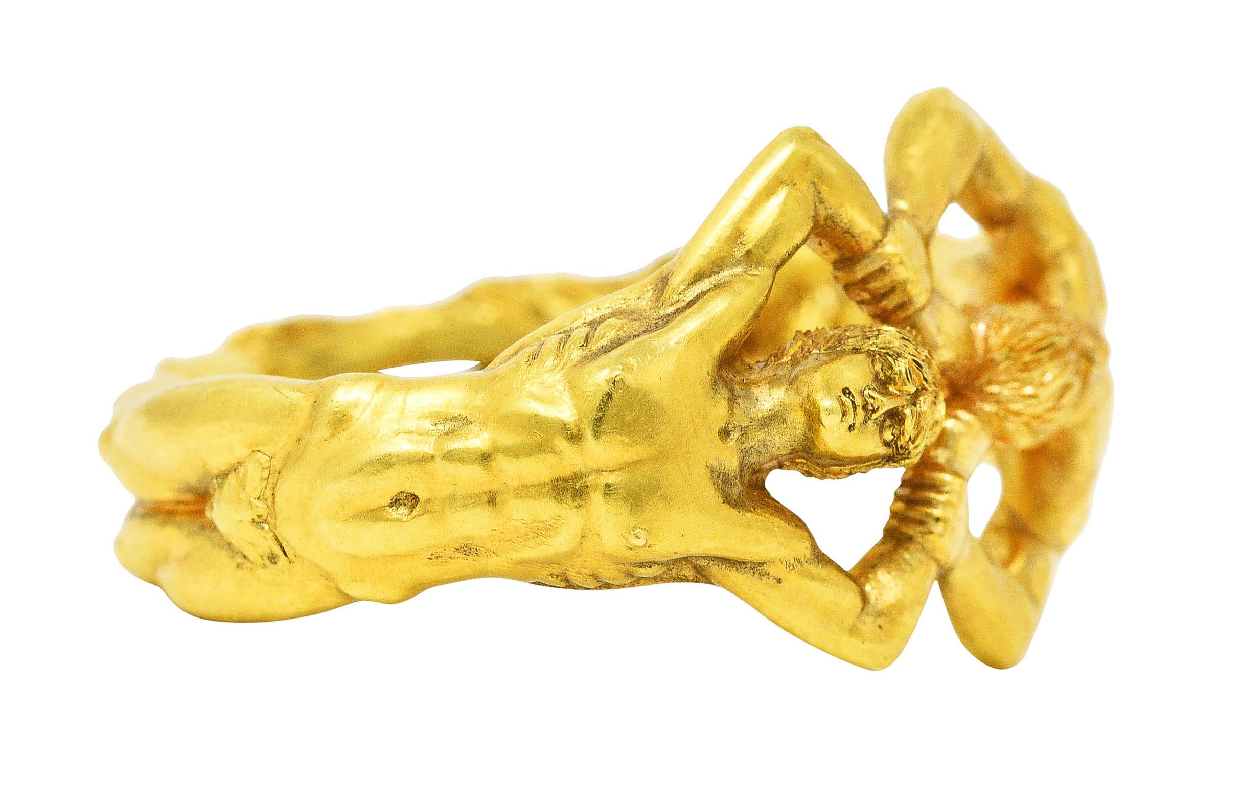 Ring is designed as two highly rendered figures - one human and one a hirsute satyr. With dramatically arched backs - figures meet hand to hand and foot to foot. Arms form a grappled buckle motif. Completed by a matte gold finish with intricate