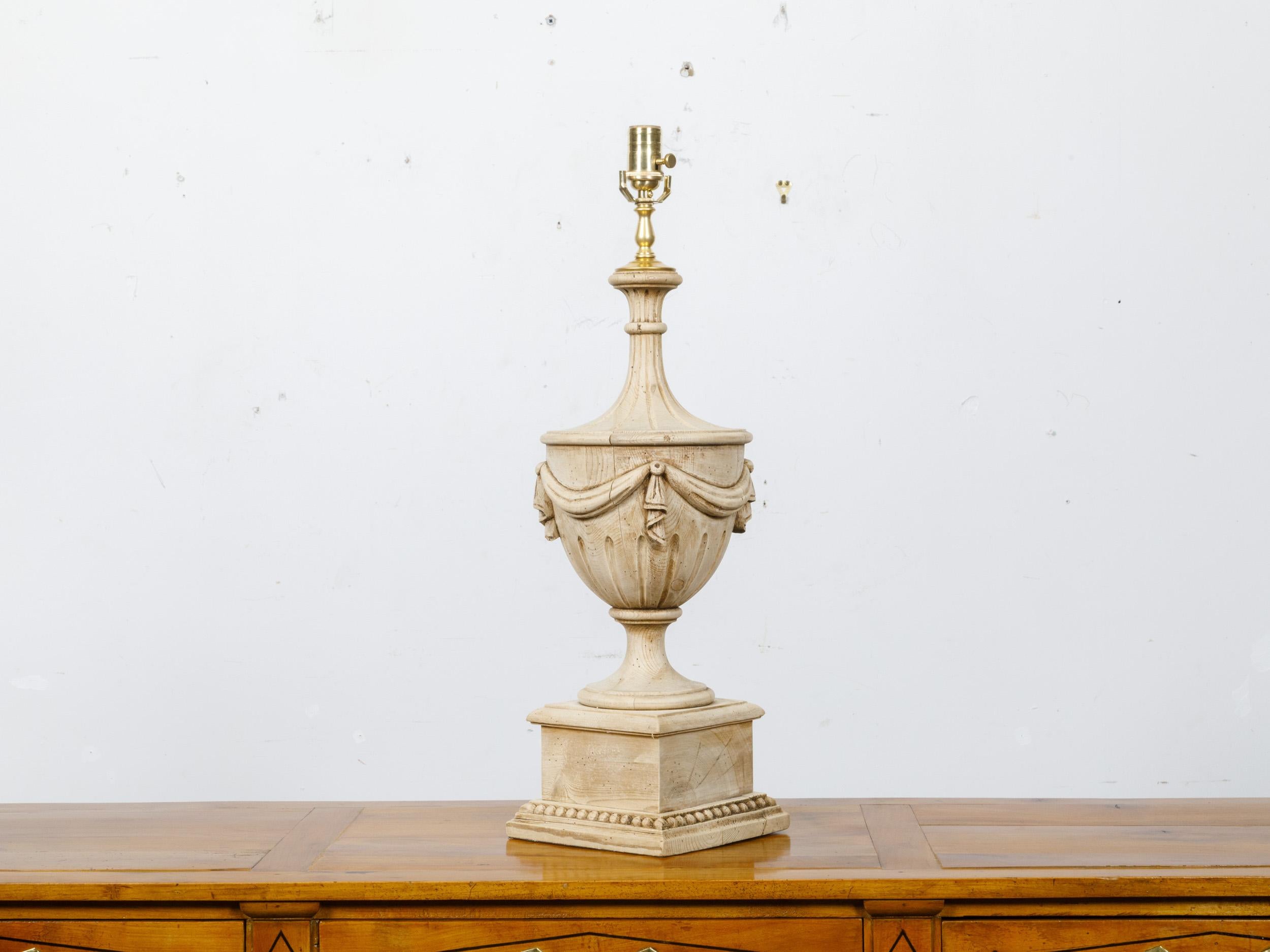 A 19th century Neoclassical carved pine urn form finial with swag motif, made into a table lamp wired for the USA. This exquisite table lamp artfully repurposes a 19th-century Neoclassical pine finial, offering a unique blend of historical