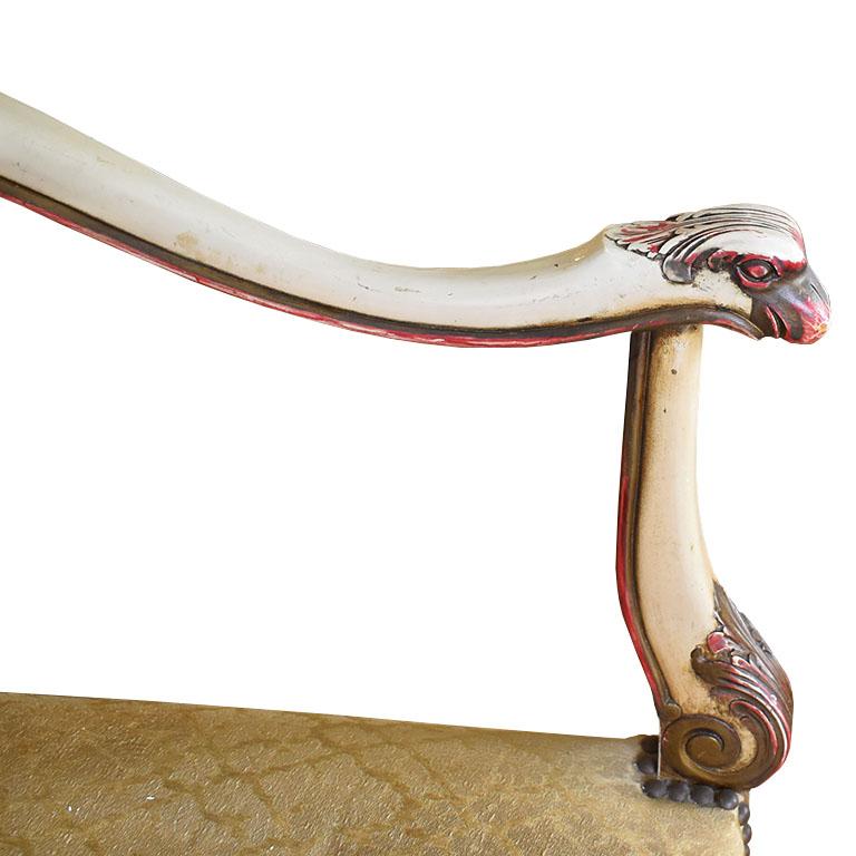A Neoclassical carved swan armchair with upholstered seat back and seat. This antique piece is created from wood and features armrests that are carved to look like swans. The seat back is rectangular and upholstered in a cream and gold fabric with