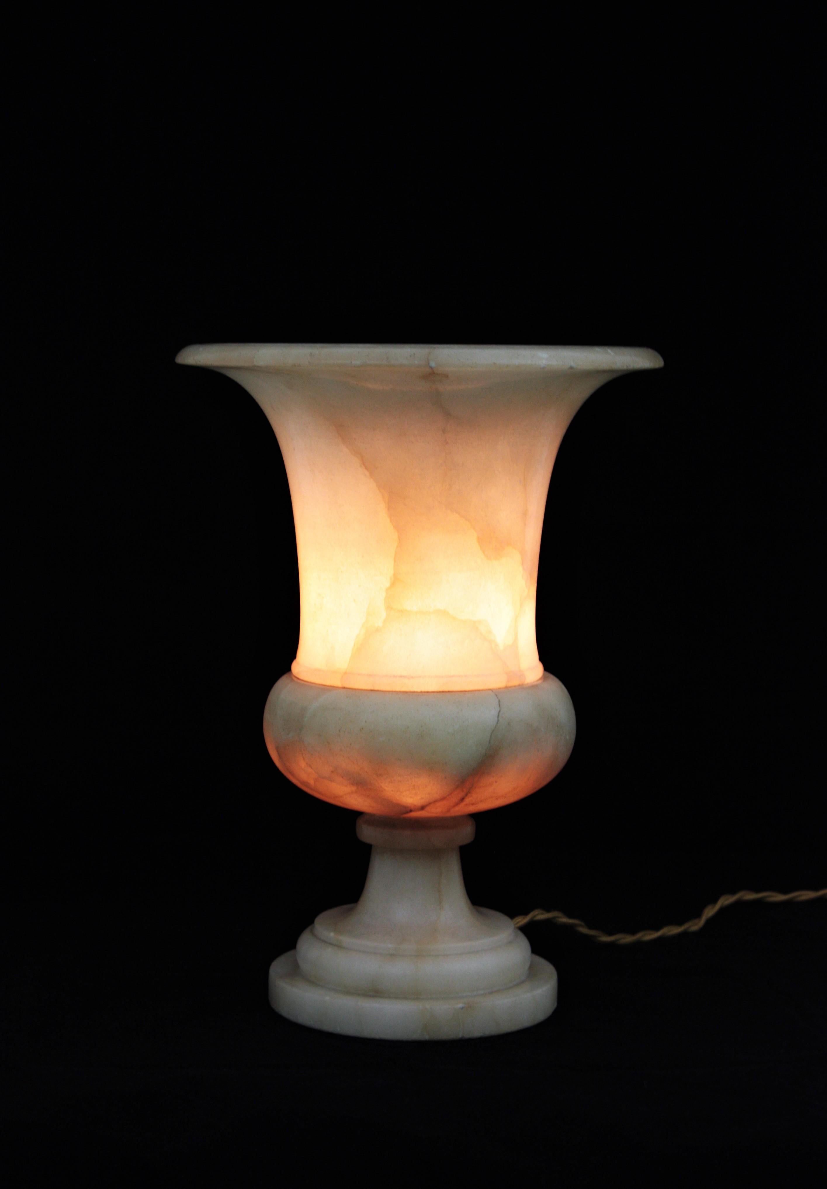 Sculptural alabaster Art Deco period urn table lamp with neoclassical design. Spain, 1930s.
Magnificent color and interesting vintage patina. It provides a charming light. Impressive appearance when it is lit.
This elegant carved alabaster