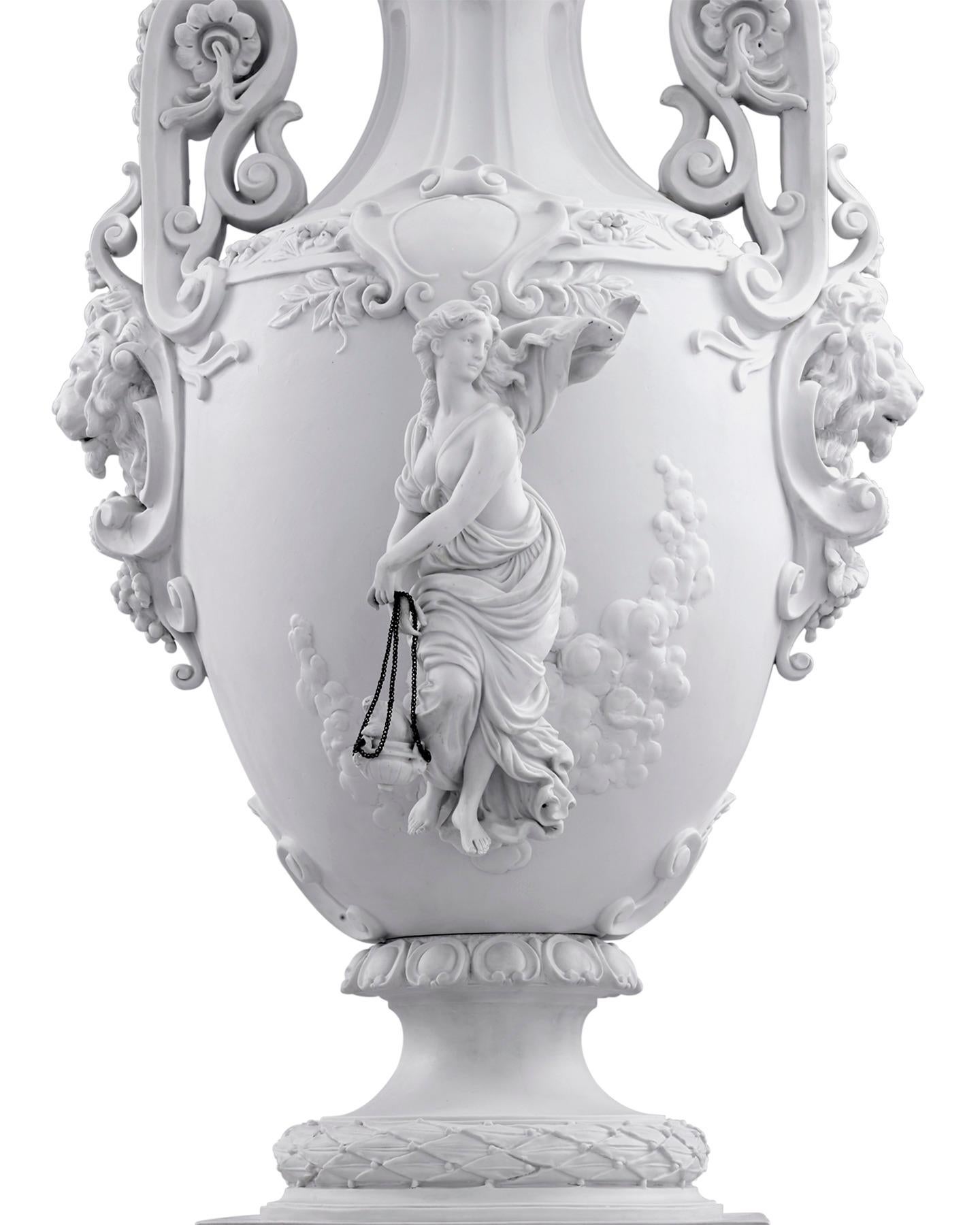 A stunning representation of the neoclassical aesthetic, this exceptional 19th century urn is handcrafted from white bisque porcelain. The impressive piece is encased by elaborate neoclassical motifs, including two female figures that recall the