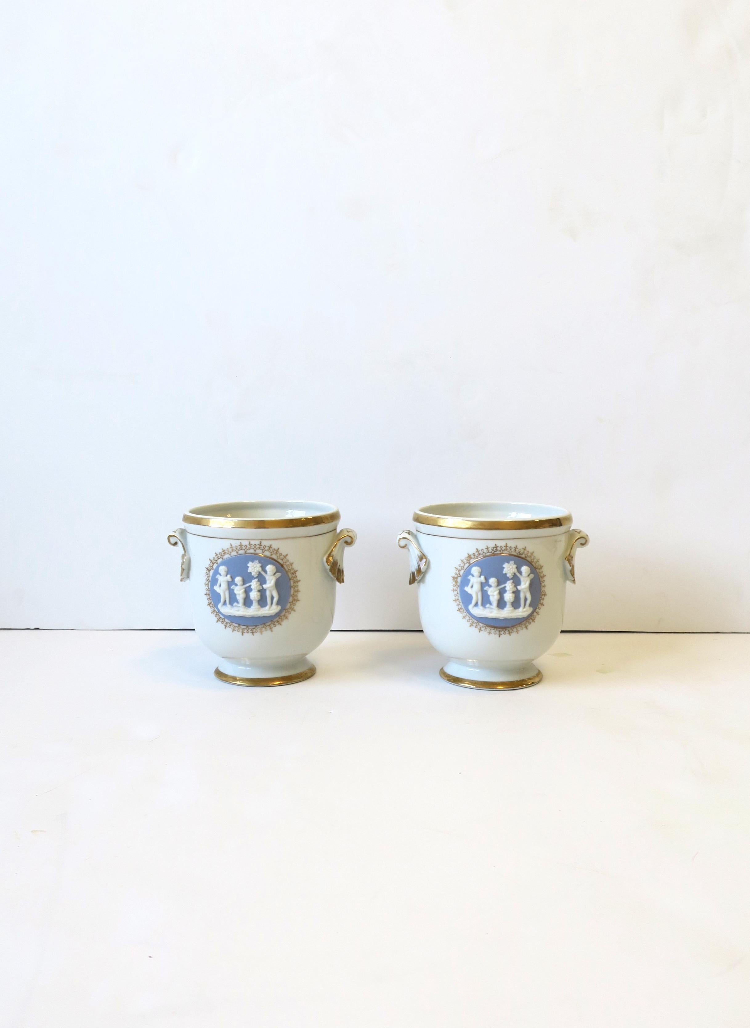 A beautiful small pair of porcelain ceramic cachepots or jardinières with neoclassical relief scene, circa early to mid-20th century, Europe. Cachepots or jardinières are white with a light blue raised relief scene on front, handles on sides, and