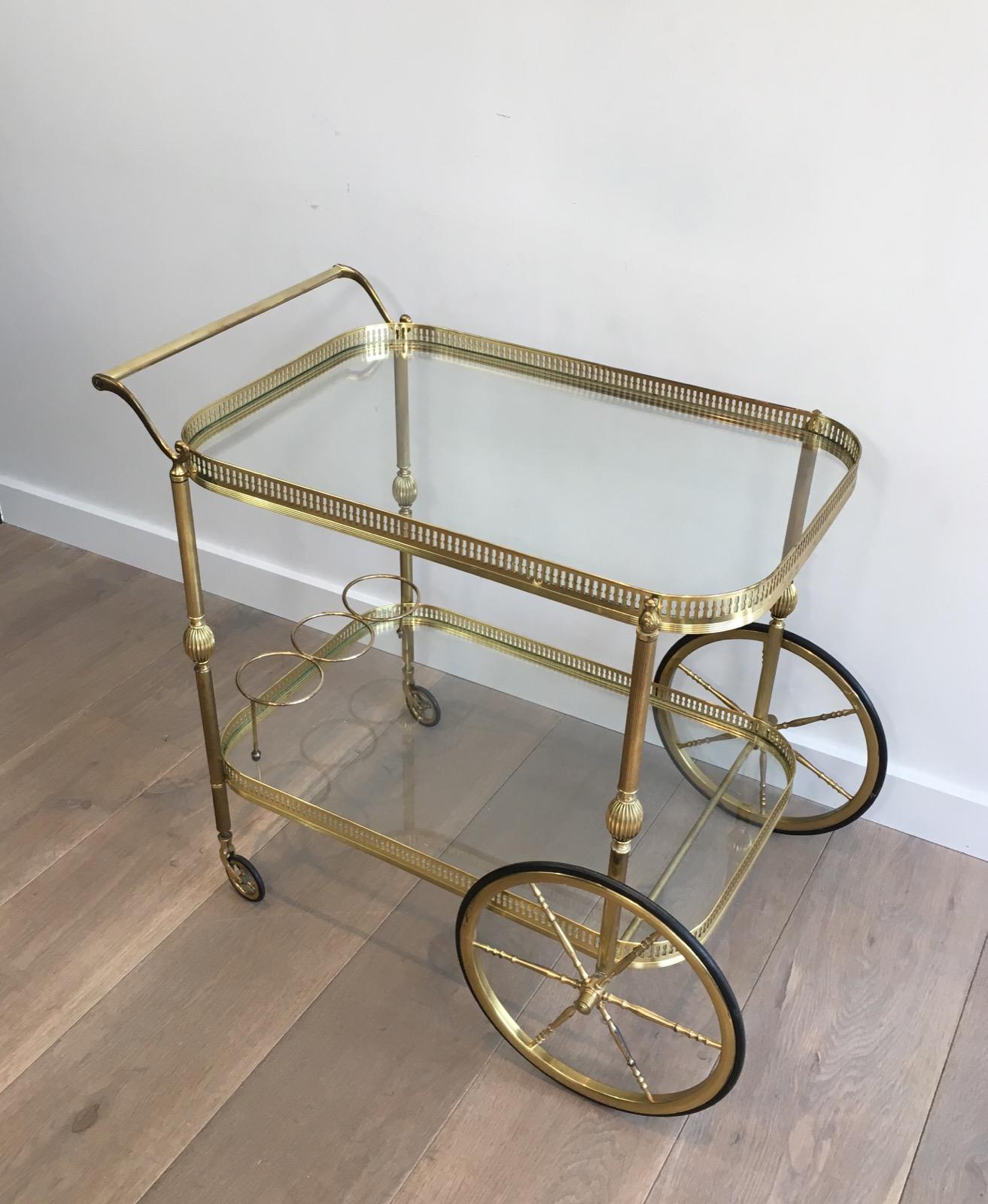 This elegant neoclassical bar cart is all made of brass with two glass shelves. This drinks trolley has nice details and its large wheels on front are very decorative. There is a three bottles holder on the bottom part. This is a French work, in the