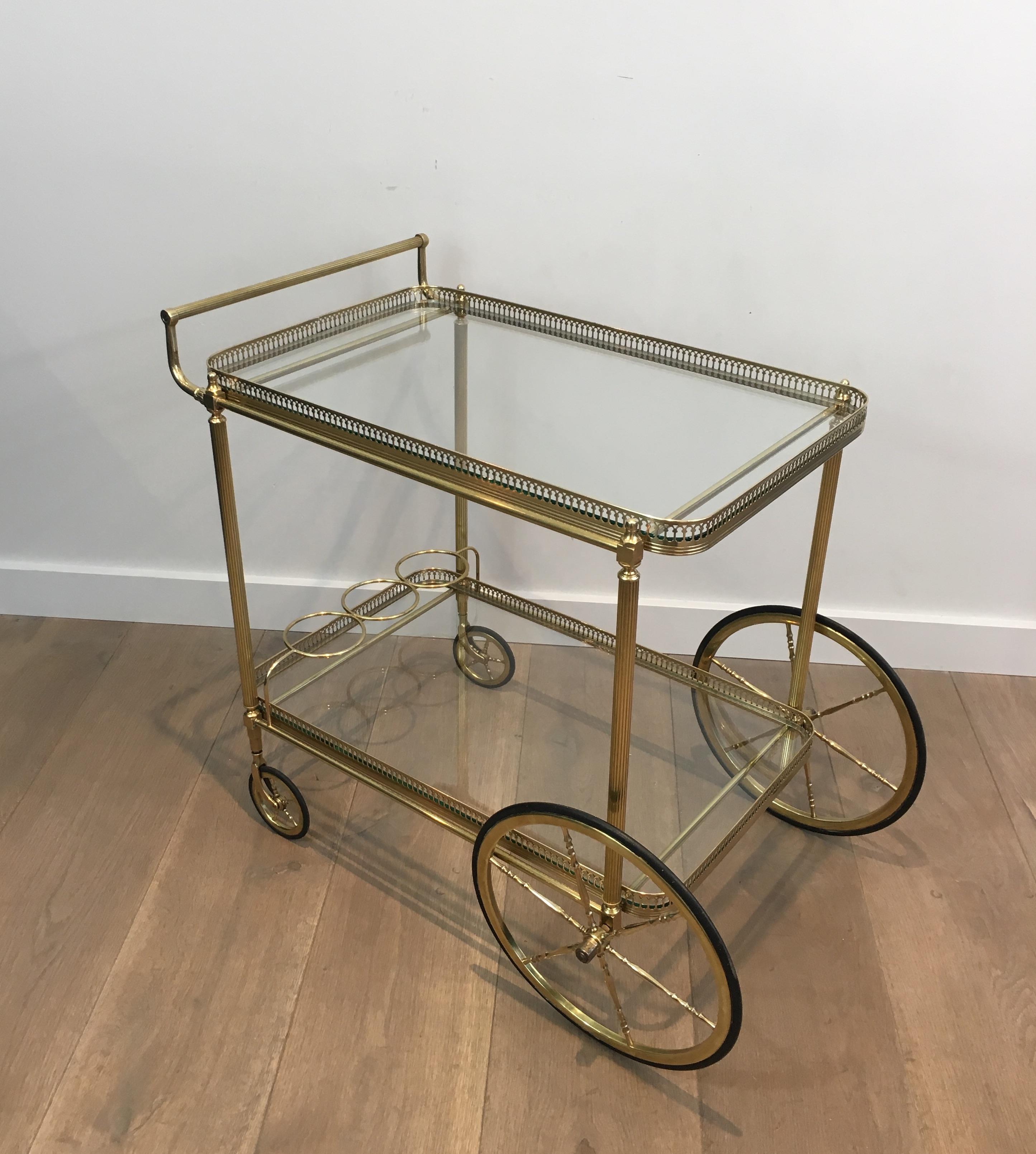 This neoclassical bar cart is made of brass with two glass shelves and two large wheels in front. This drinks trolley is a French work, circa 1940.