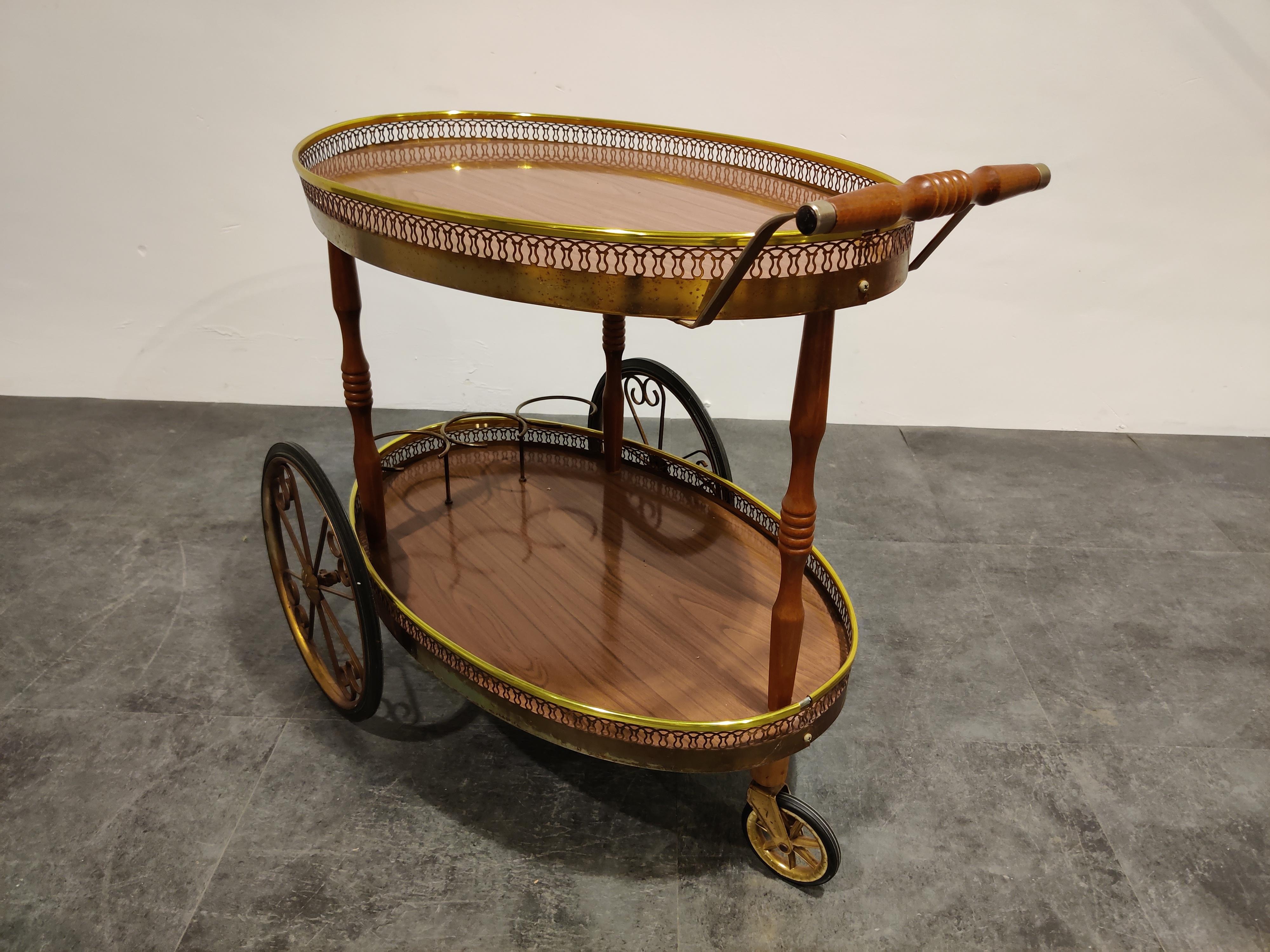 Elegant midcentury neoclassical style serving trolley.

Beautiful brass details and two tiered veneer wooden trays.

Three bottle holders and enough space for glasses and other.

1960s, Italy

Good condition with normal age related