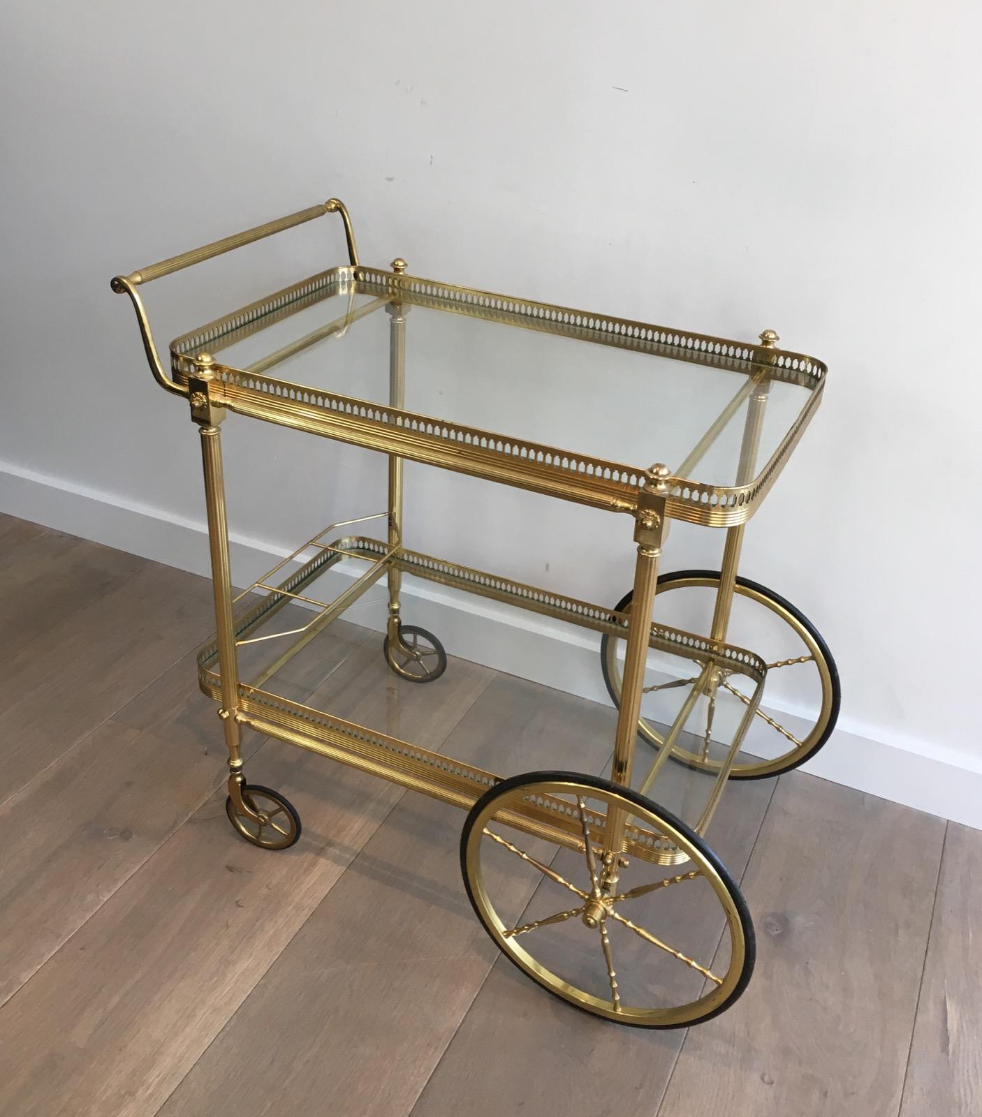This neoclassical drinks trolley is made of brass with 2 glass shelves and a bottle holder on the bottom part. This is a French work, in the style of Maison Jansen, circa 1970.