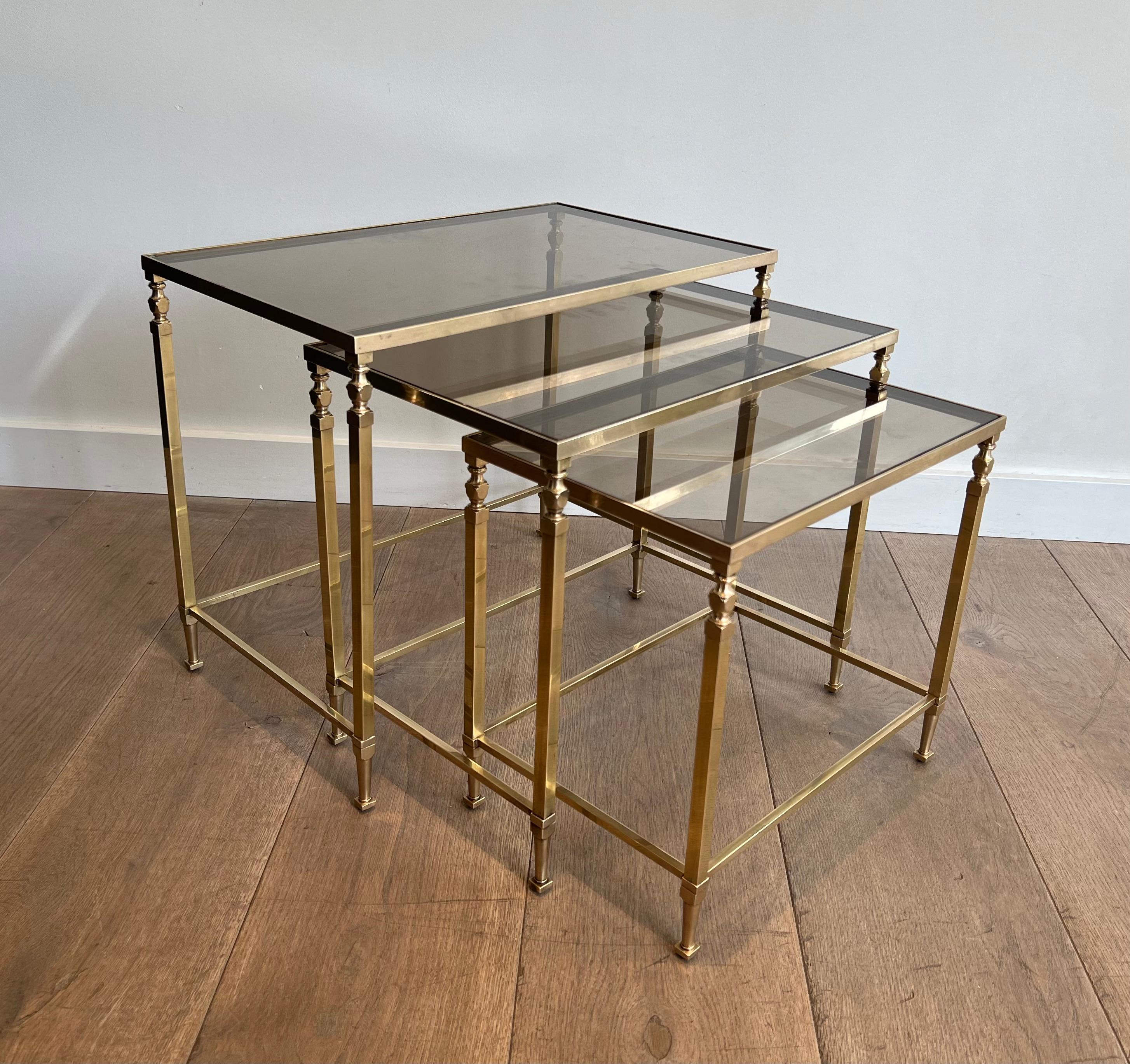 Ces tables gigognes de style néoclassique sont fabriquées en laiton avec des étagères en verre fumé. Il s'agit d'une œuvre française du célèbre designer Maison Ramsay. Circa 1940