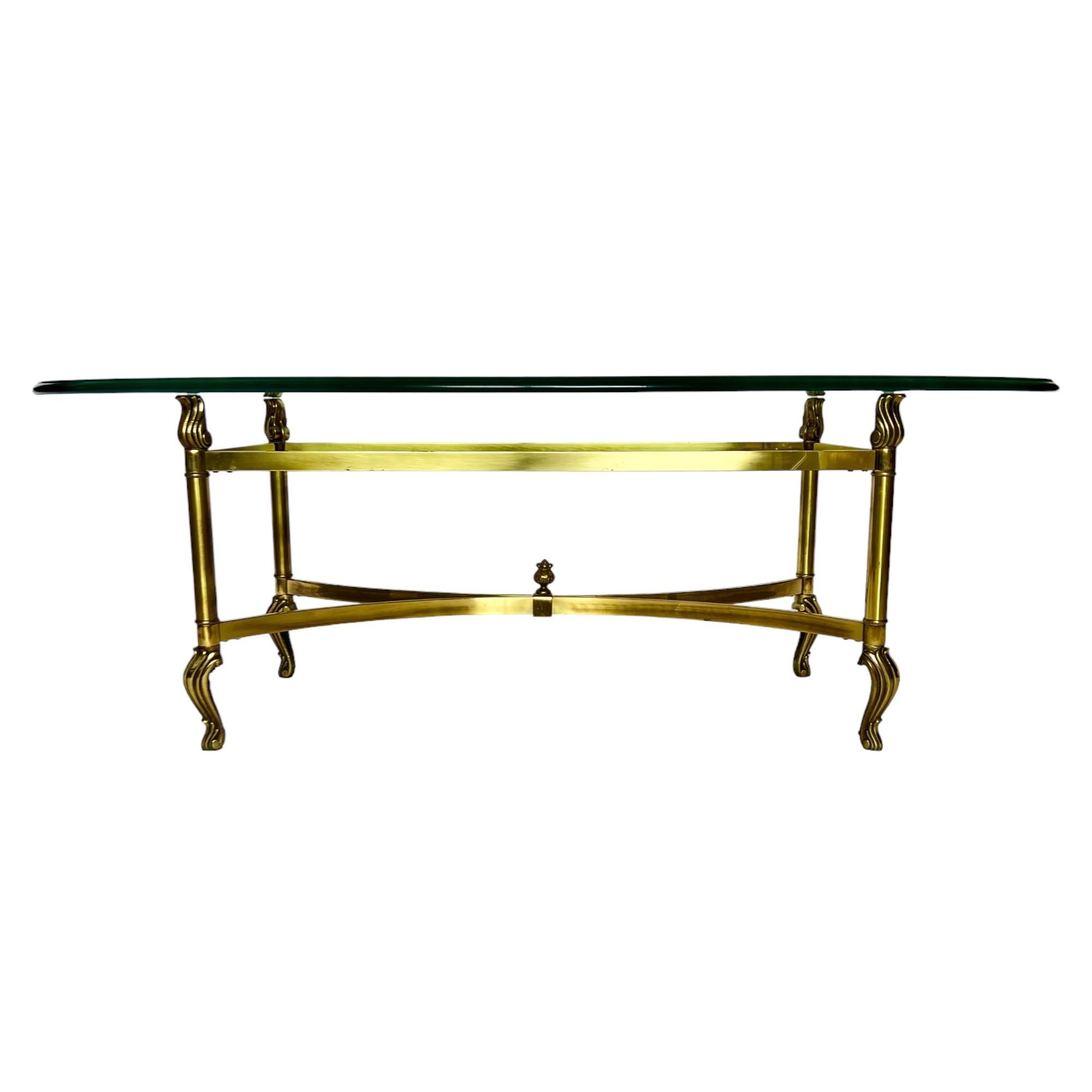 A vintage late 20th century Hollywood Regency style brass cocktail table with an oval beveled edge glass top surface of approximately 3/4 inch thickness.

Dimensions: 49.5