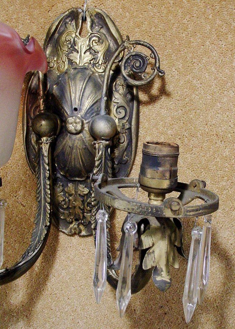 Aplique de pared neoclásico con un par de brazos de latón emplumados que se extienden desde un soporte de pared con motivos florales. El motivo floral continúa en toda la pieza. El candelabro presenta un par de pantallas de cristal de pañuelo teñido