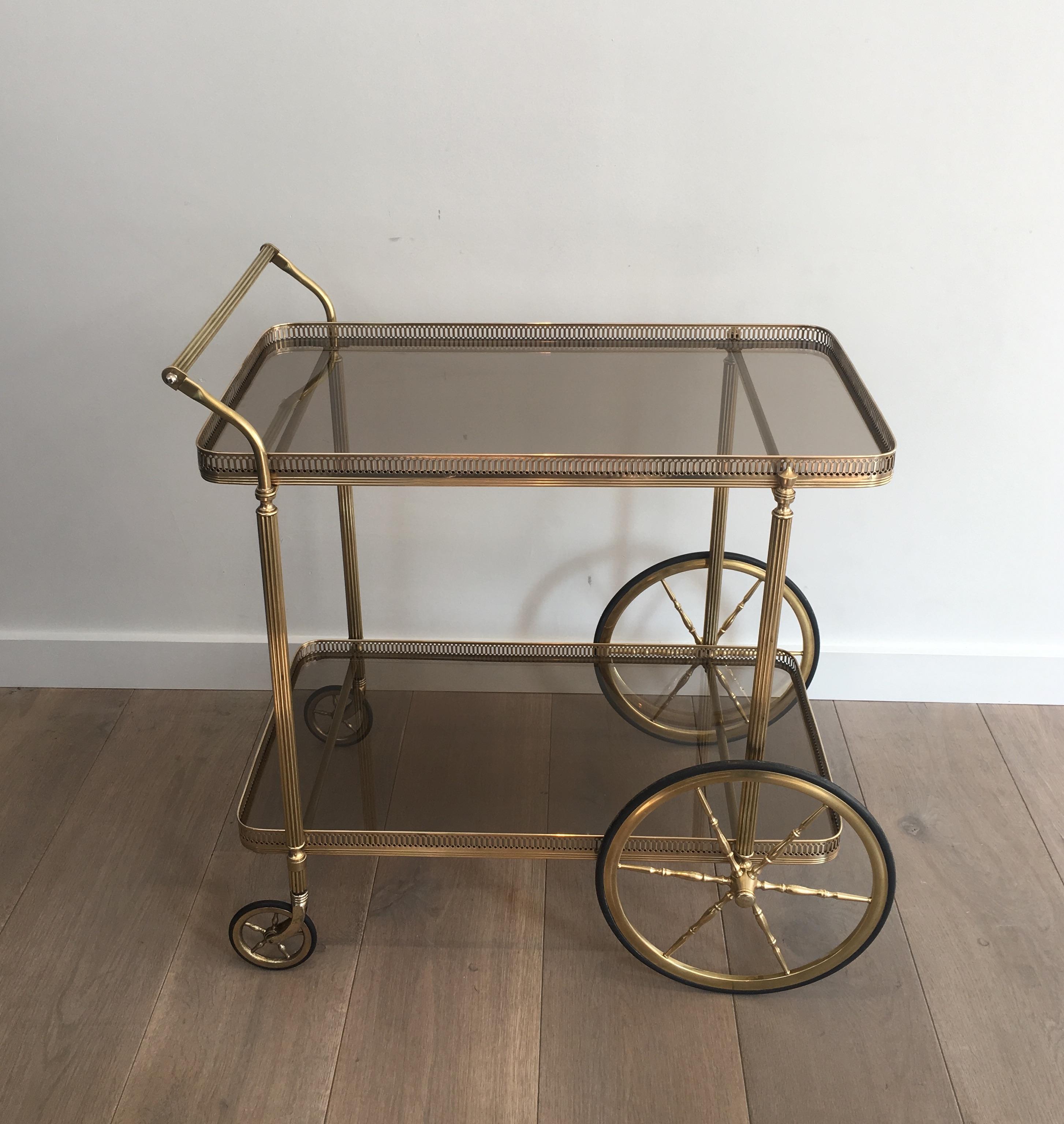 This neoclassical style brass bar cart is made of brass with smoked glass shelves. This is a French work in the style of famous French designer Maison Jansen, circa 1940.