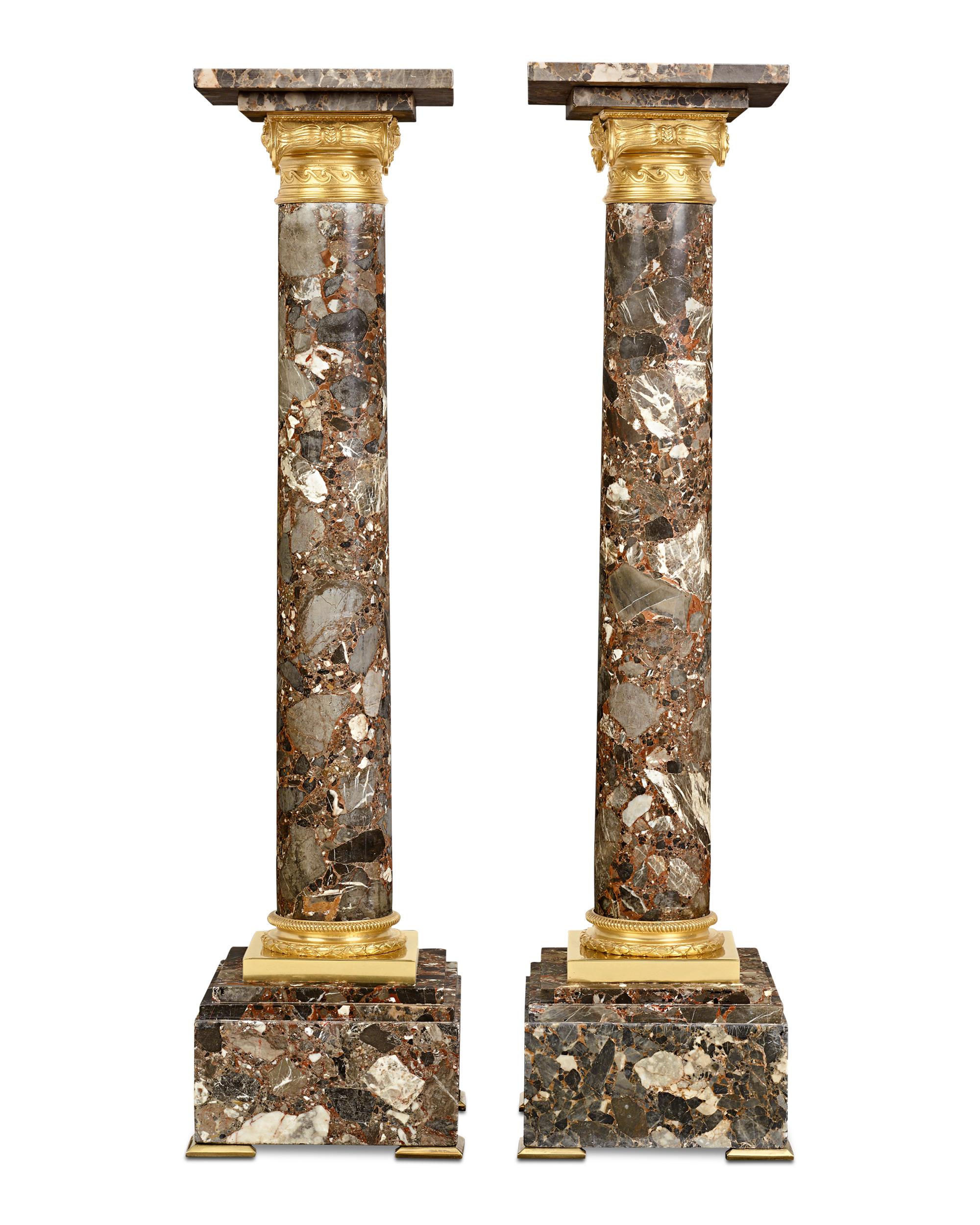 A classic Neoclassical style sets apart this stately pair of Breccia marble pedestals. Taking the form of Ionic columns with brilliant ormolu capitals and bases, the impressive pieces can serve as display pedestals or as stunning sculptures in their