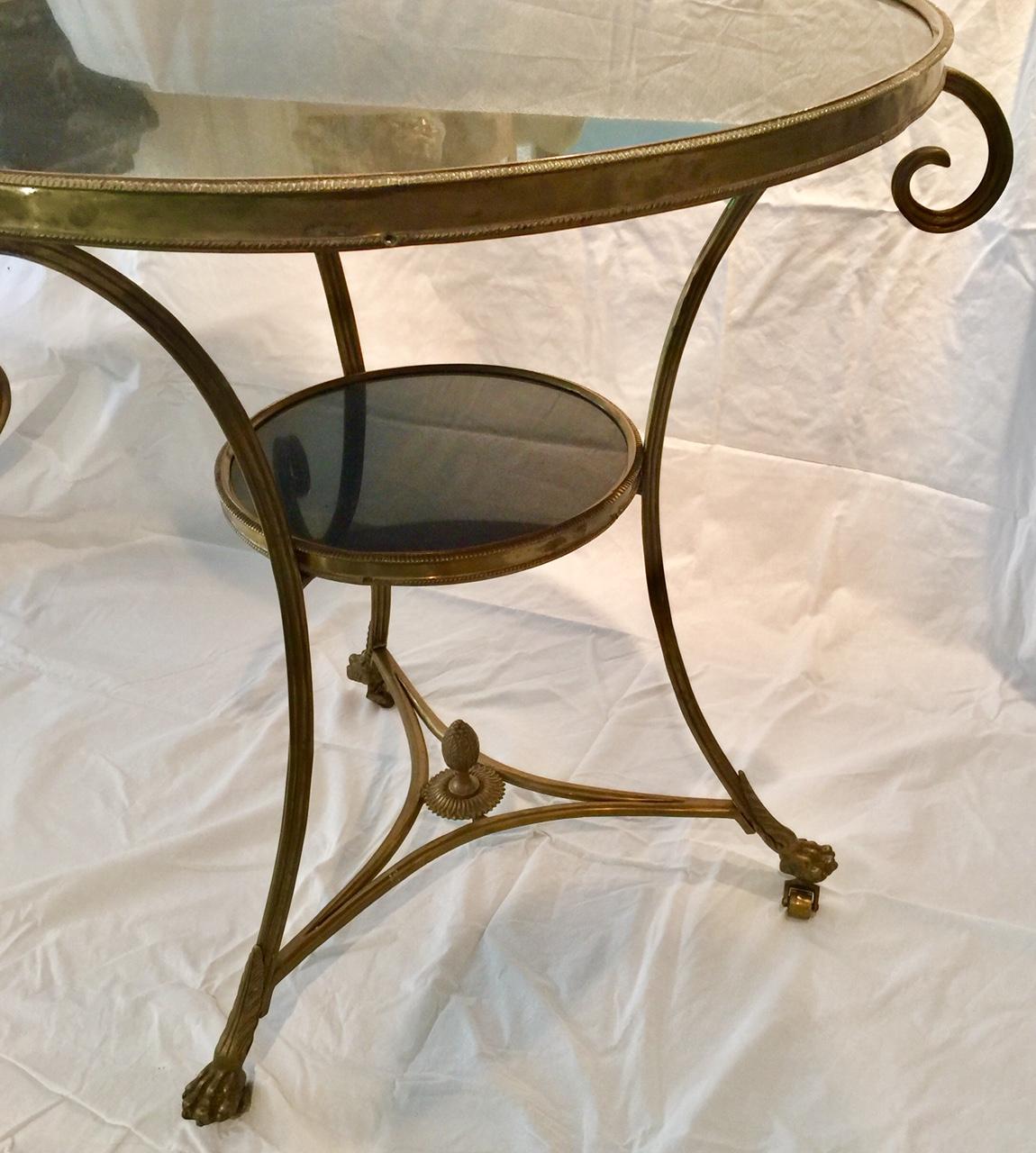 A classic French bronze and black marble two-tiered round gueridon table on scrolled legs with paw feet on castors. A round black marble top is encircled by a decorative bronze band. The legs are joined by an openwork triangular bronze crosspiece,