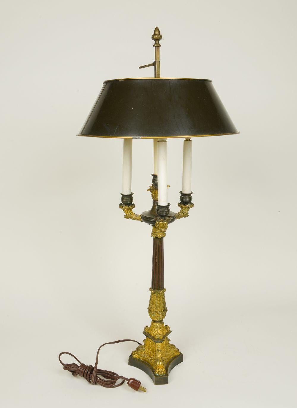 Of columnar form enriched with acanthus leave decoration, issuing three candlearms fitted with electrified candlesleeves, on a tripartite plinth base; with black and gilt tôle shade.