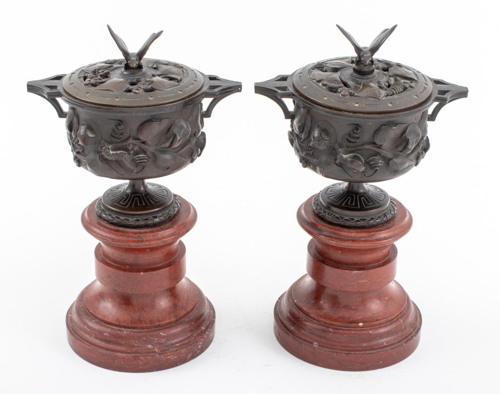 Pair of Neoclassical Grand Tour patinated bronze covered tazza urns cast with floral decoration to bowls on bases with Greek Key borders, the pierced lids with ivy motif and surmounted by butterfly-form finials, framed by two handles, mounted on
