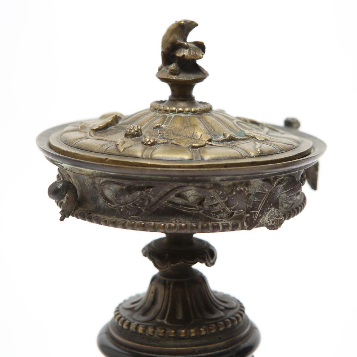 Neoclassical bronze covered tazza urns, cast with high-relief leaves and berries motif, with handles, the base with bead-work and the black marble plinths with applied bronze relief rondo of classical figures. One cover slightly misshapen and one