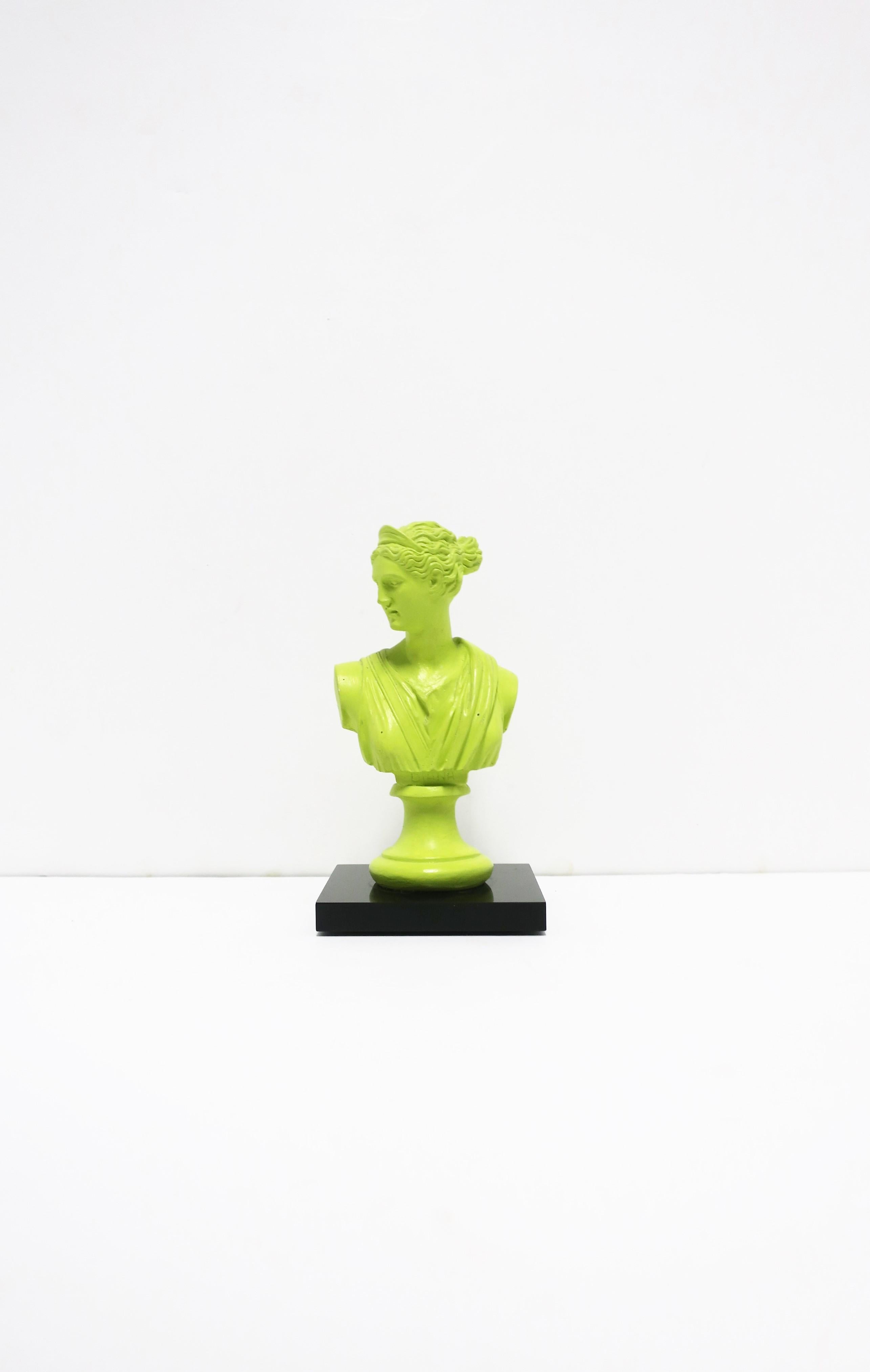 A neoclassical female bust statue in neon green on a black glass base. This is a resin or composite bust statue adhered to a square black glass base. A great pop of color for a bookshelf, office, desk, etc. Dimensions: 3.5
