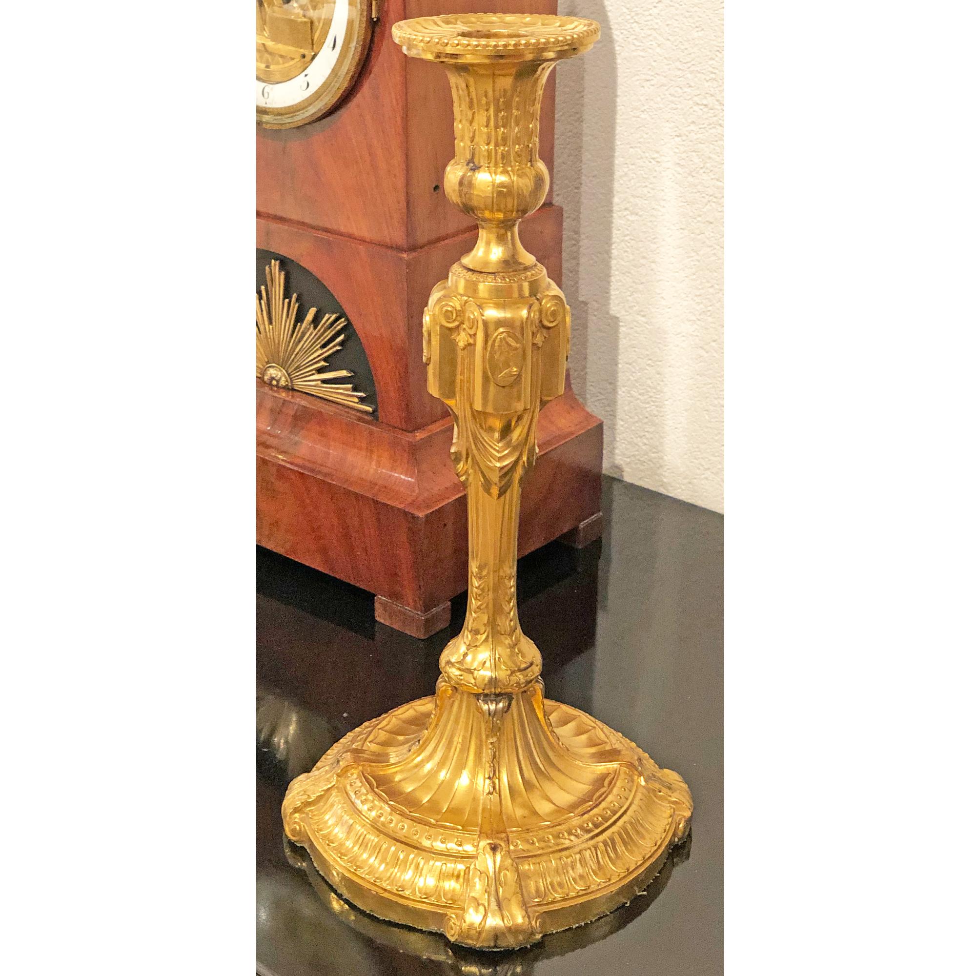 Pair of gilt candlesticks with neoclassical decor and scrolls. The shaft is decorated with cameos.