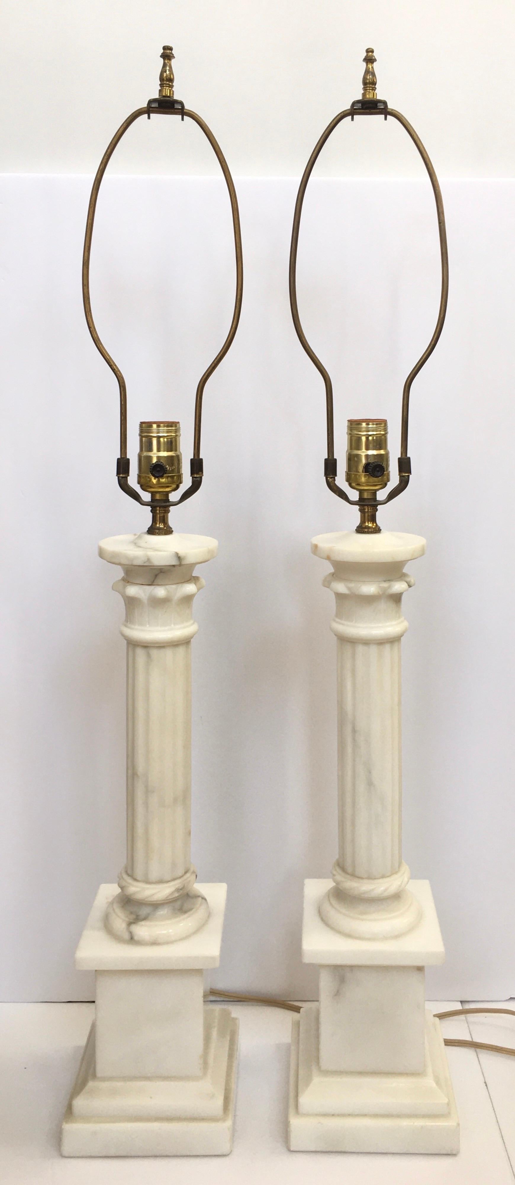 Pair of classic neoclassical style 'ionic column' solid marble pillar table lamps. These tall buffet lamps feature polished white marble with grey veining. Beautifully carved fluted columns are mounted on square plinth bases. Lamp shades not