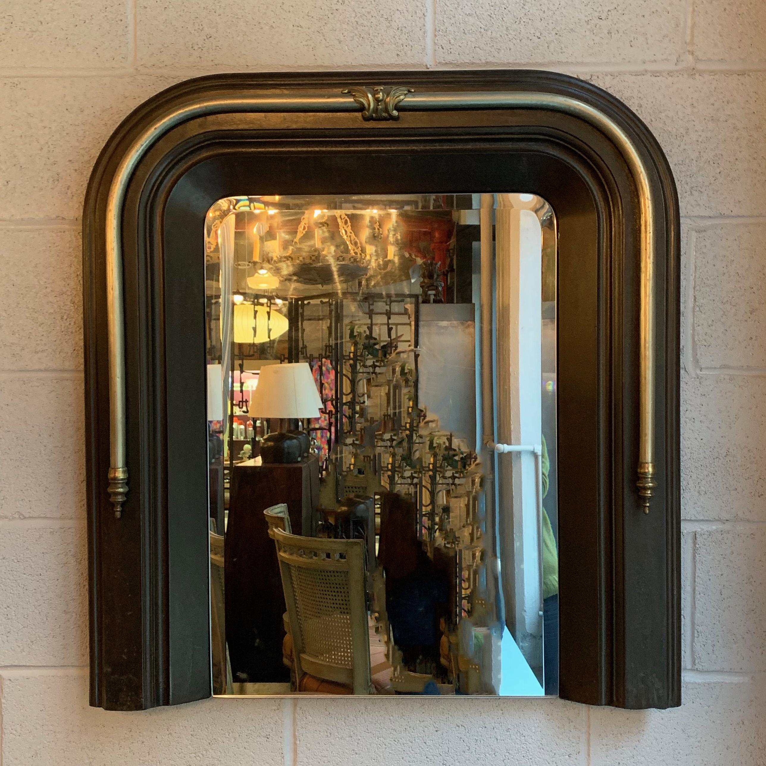 Custom wall mirror features an antique, neoclassical, cast iron and nickel plated fireplace surround with brass accents and beveled mirror.