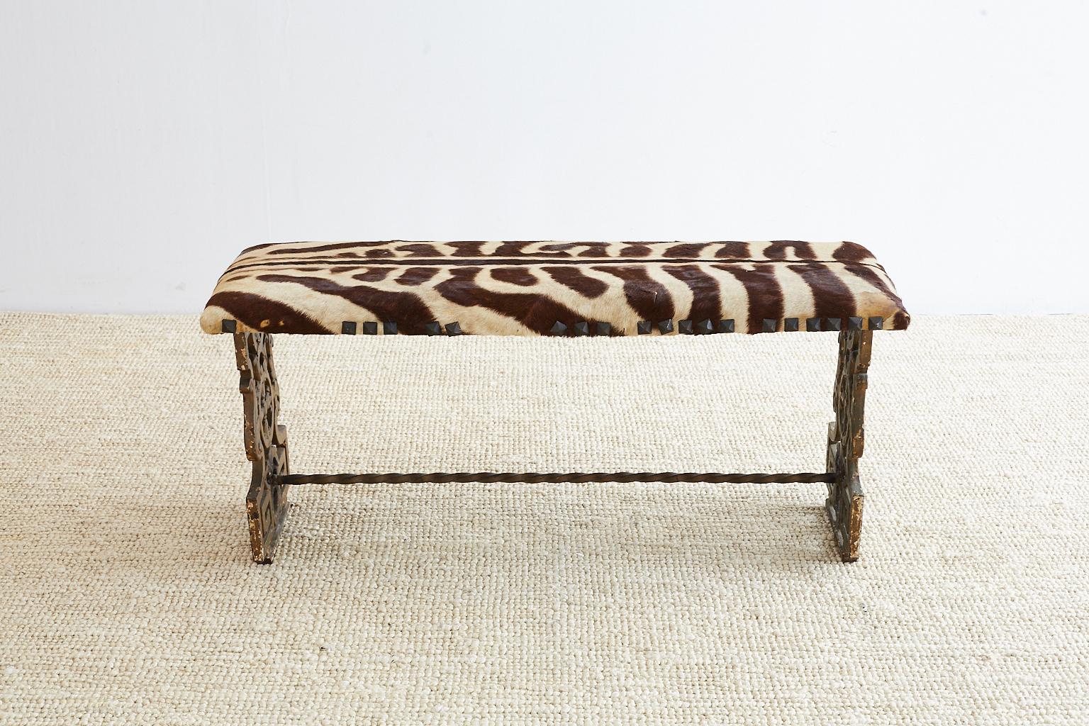 Fabulous cast iron vanity bench made in the neoclassical taste featuring a vintage zebra leather hide upholstery. The two legs have a Greek key motif and a distressed painted finish. Conjoined with a twisted iron stretcher and supporting bench seat