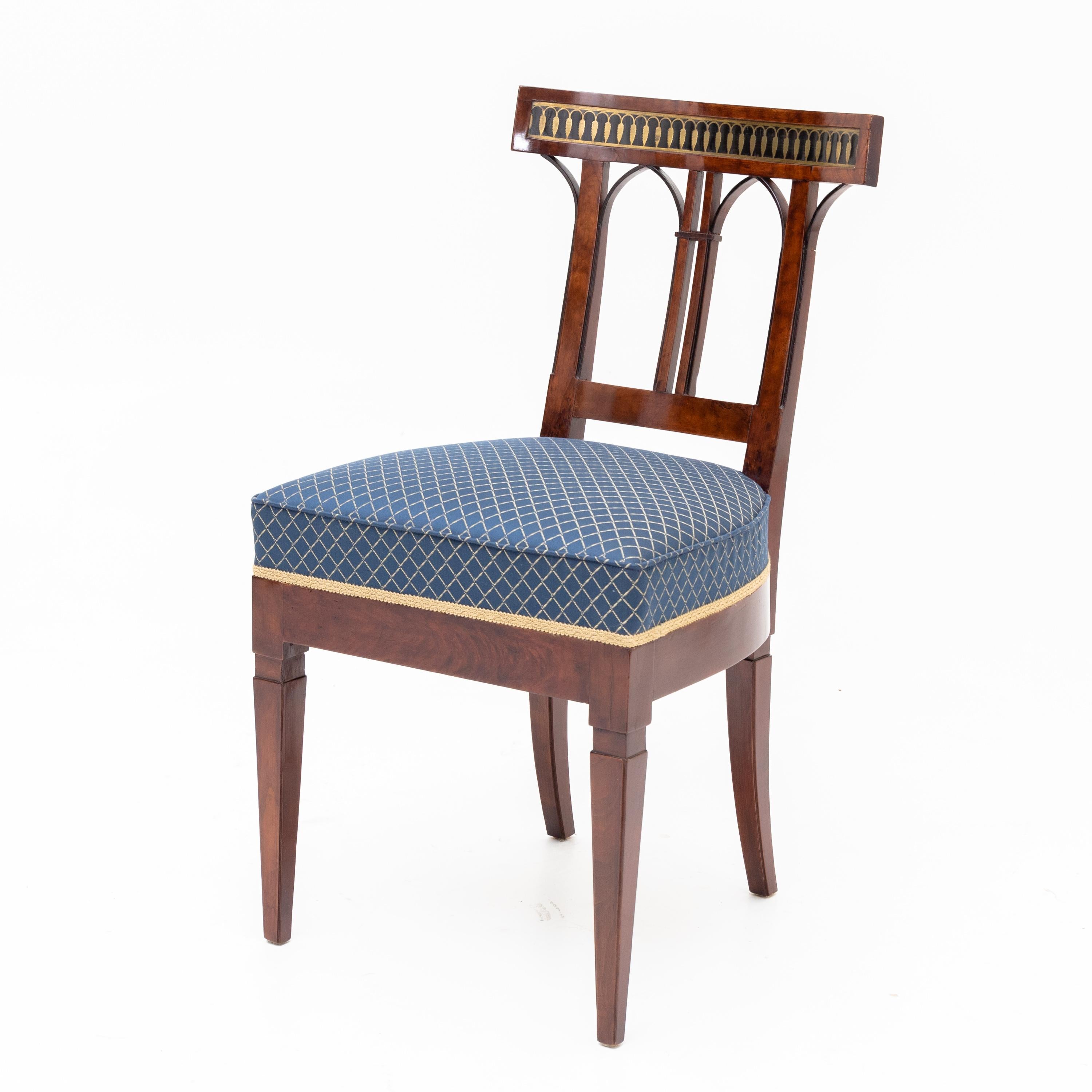 Sedia neoclassica su gambe quadrate a punta con struttura dritta e sedile trapezoidale imbottito e schienale traforato con archi a sesto acuto stilizzati e intarsi in ottone a forma di arcate e spighe di grano. La sedia è stata rivestita di recente