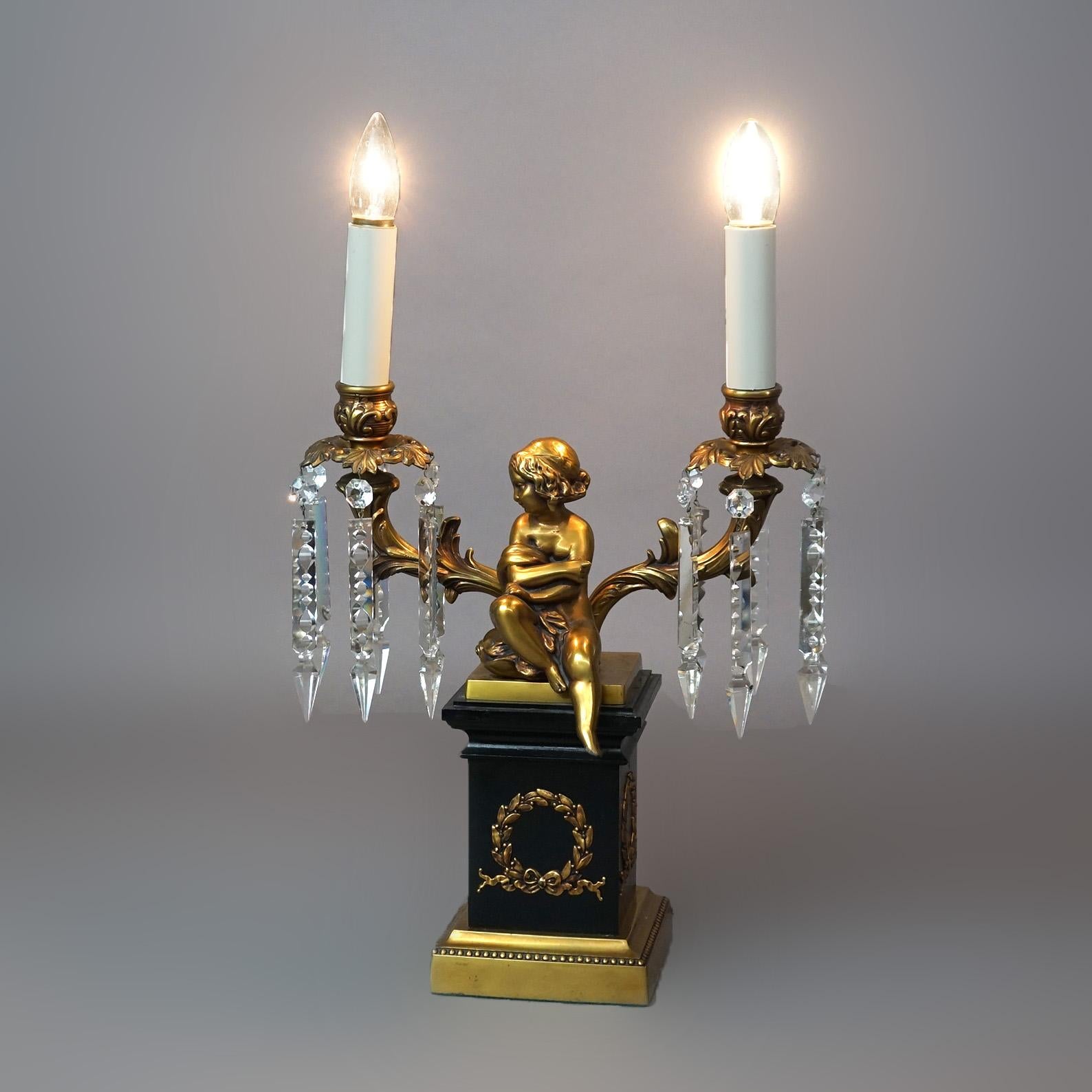 A Neoclassical figural cherub lamp offers brass and ebonized metal construction with two arms terminating in candle lights, 20th century

Measures - 22.5