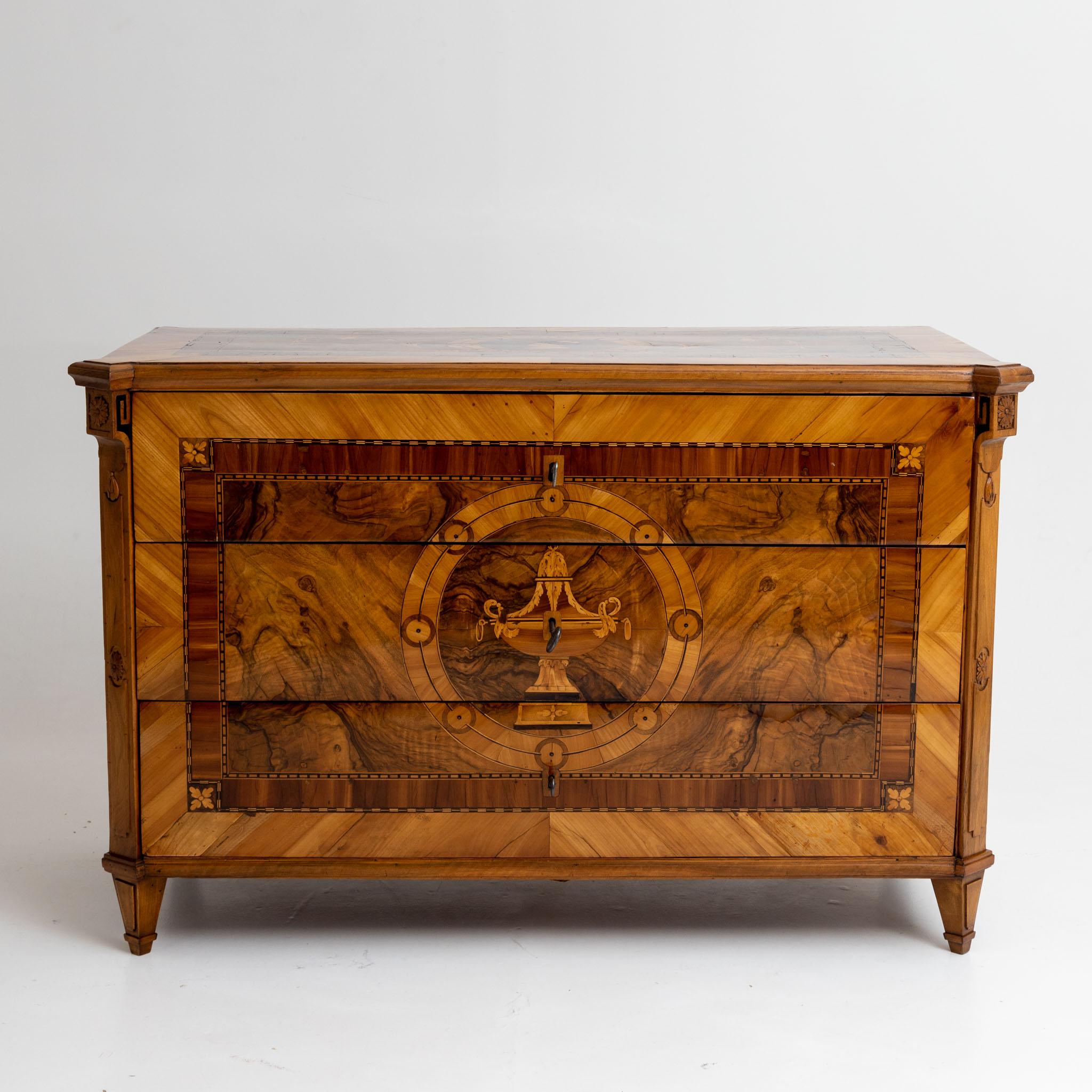 Large neoclassical chest of drawers on square-pointed feet, veneer and marquetry in cherry and walnut. The body is decorated with openwork volutes with rosette decoration on the beveled corners and shows framing inlays on all sides. On the front is