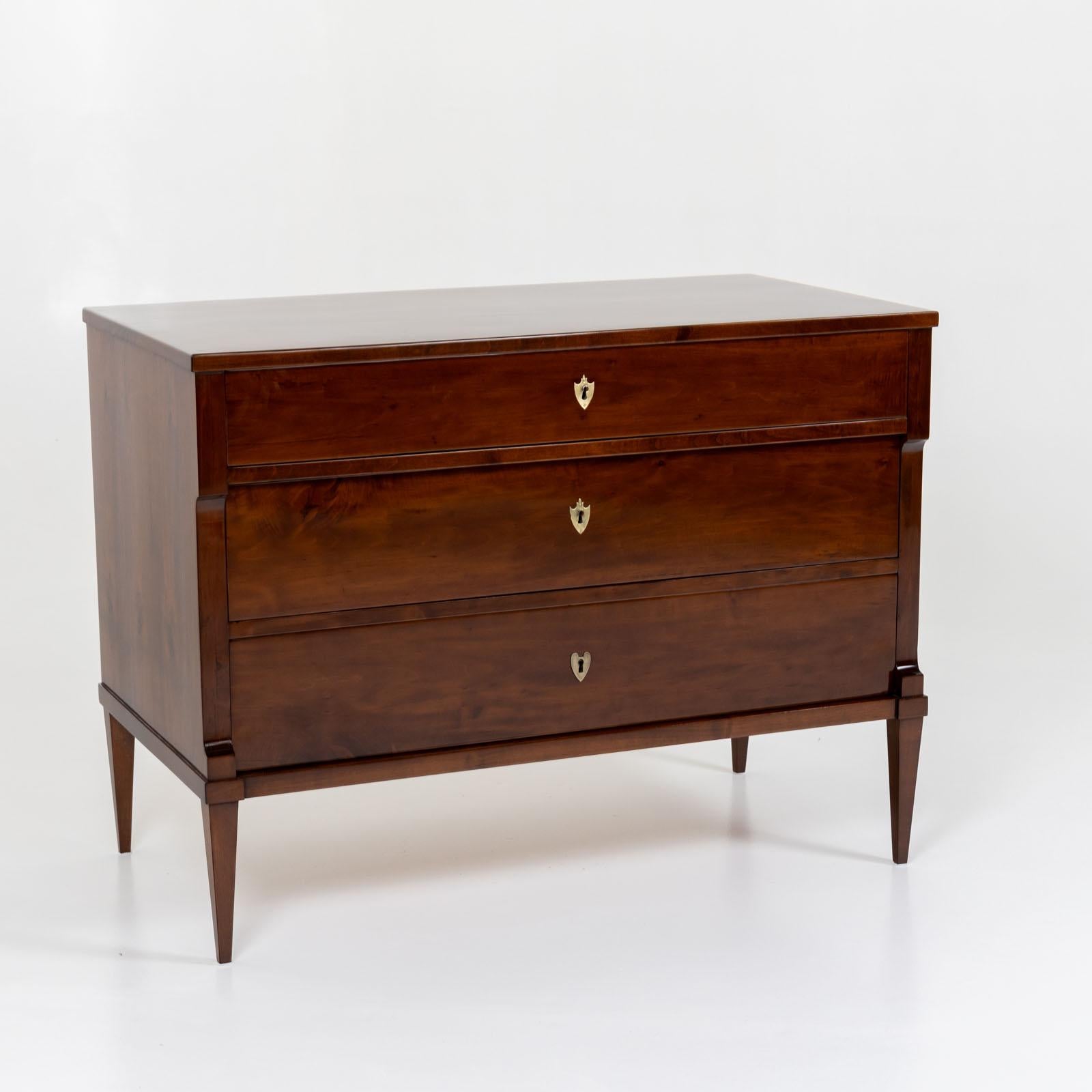 Neoclassical chest of drawers with three drawers and brass escutcheons. The chest of drawers is made of walnut and stands on elegant square tapered legs. The top drawer is slightly shallower than the lower drawers. The pilaster strips are