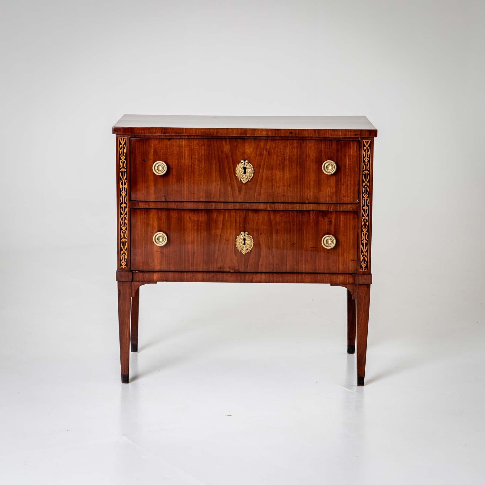 Cassettiera neoclassica compatta con due cassetti, accessori in bronzo e alte gambe affusolate. Le lesene della cassettiera sono decorate con fasce di acero intarsiato su sfondo nero. La cassettiera è stata restaurata e lucidata a mano. 