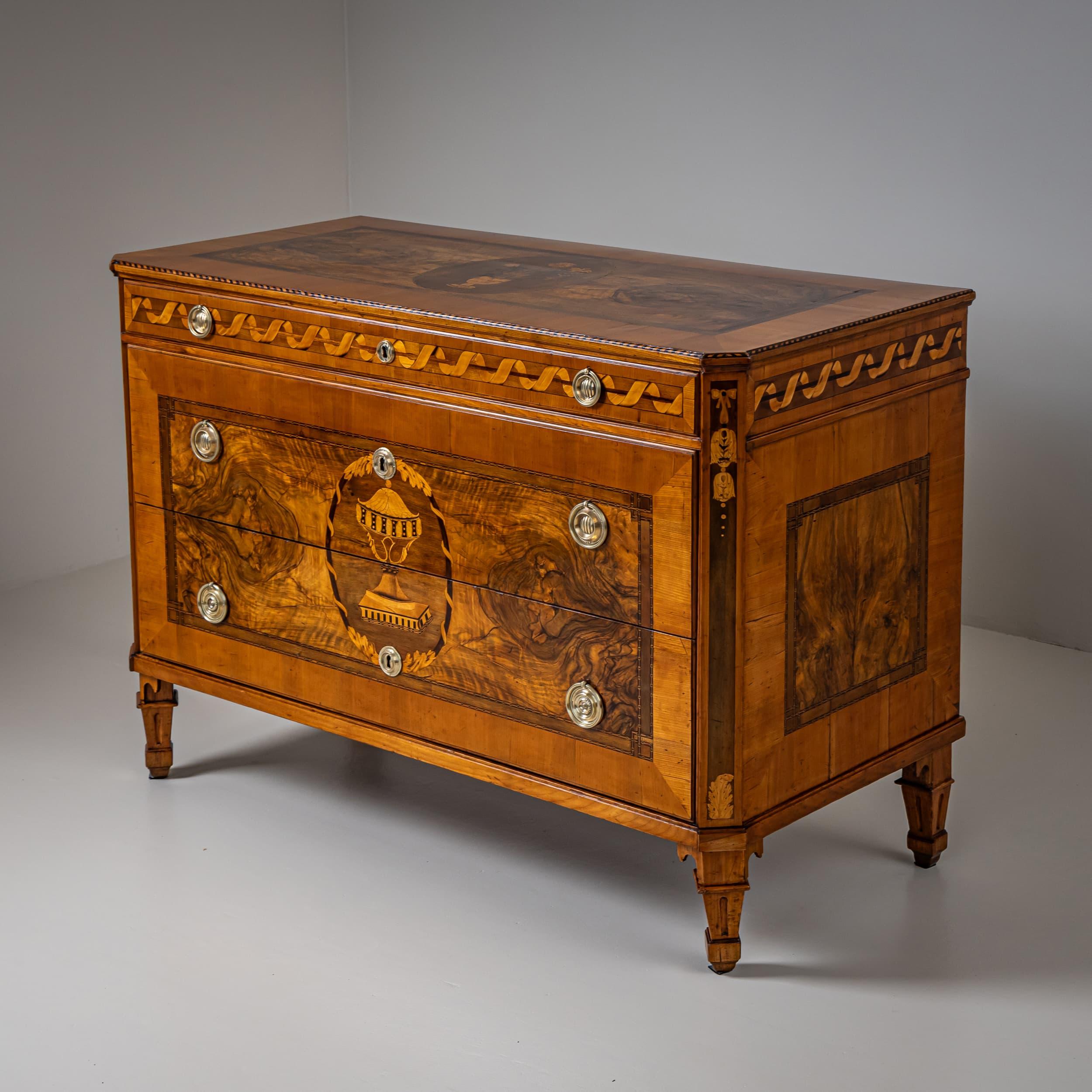 Large neoclassical chest of drawers in cherrywood with three drawers, resting on finely crafted tapered legs and featuring chamfered, slightly protruding corners. The top drawer is narrow and adorned with a marquetry wavy ribbon design. The two