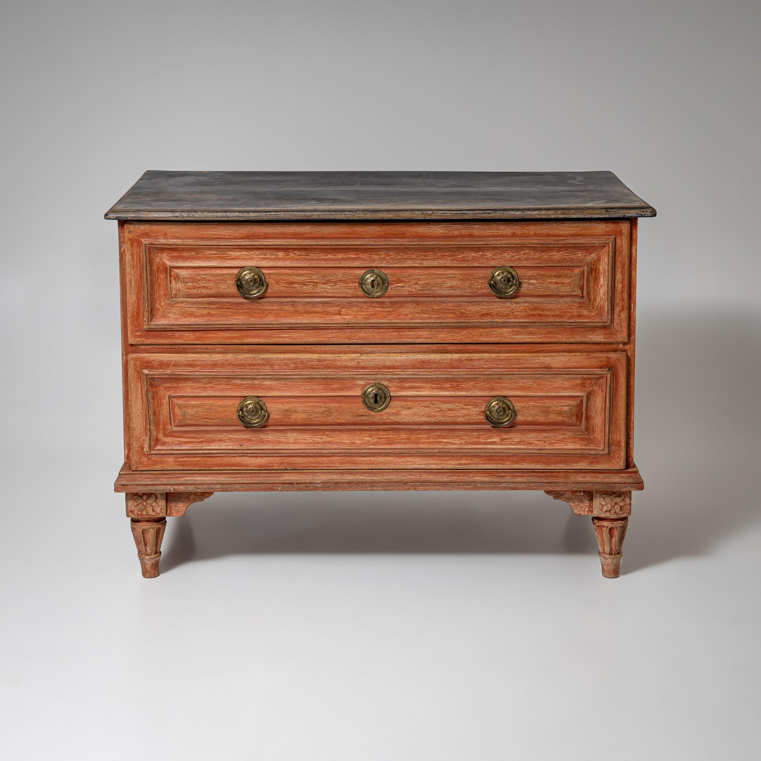 Commodo neoclassico con due cassetti e accessori rotondi in ottone, montato su gambe affusolate e scanalate. La finitura rosso mattone è nuova e anticata con patina. La piastra superiore è di colore grigio scuro.