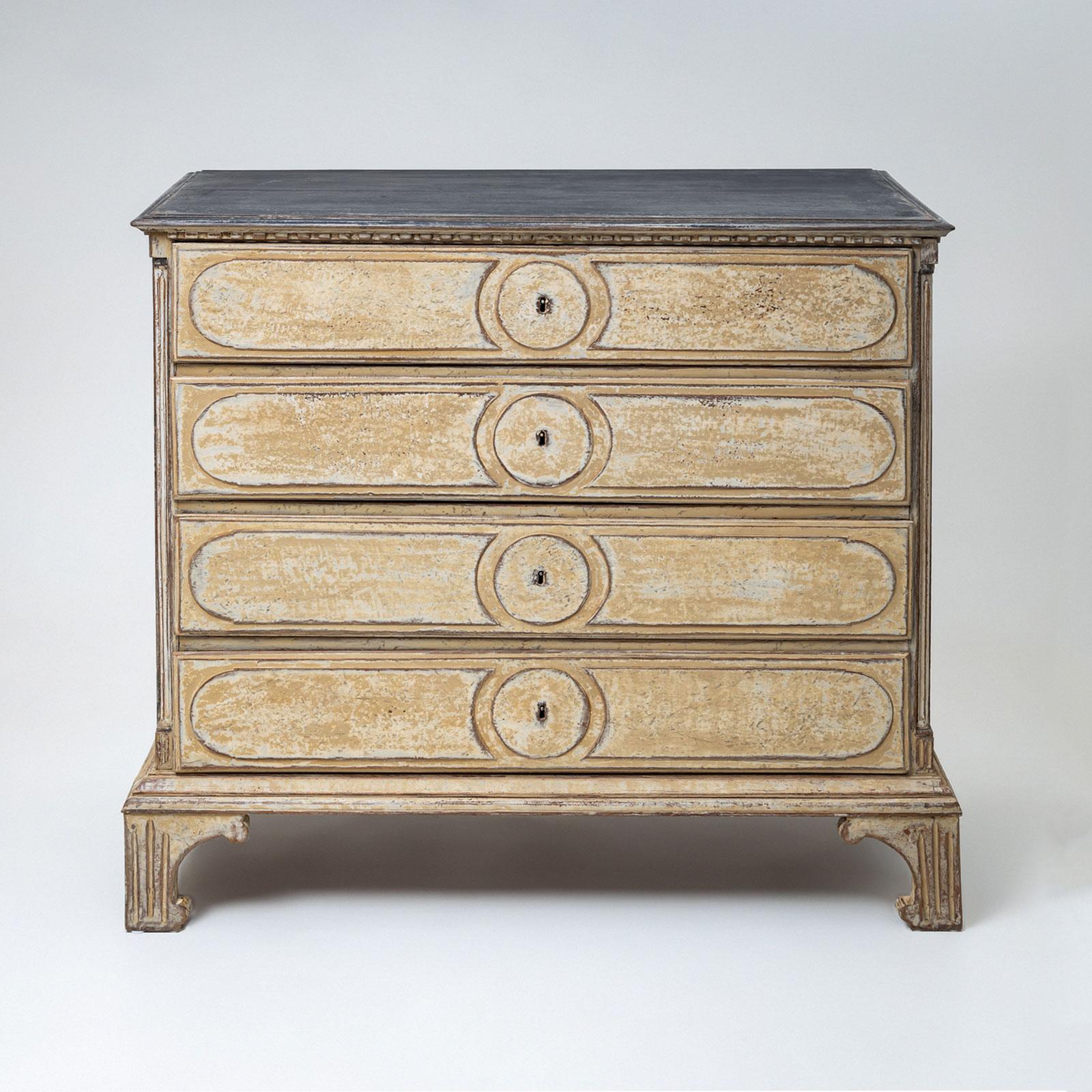 Grande commode néoclassique à quatre tiroirs avec des quarts de colonnes aux angles, reposant sur des pieds cannelés et découpés. Les façades des tiroirs sont décorées de panneaux arrondis. La commode a été repeinte dans une couleur beige et patinée