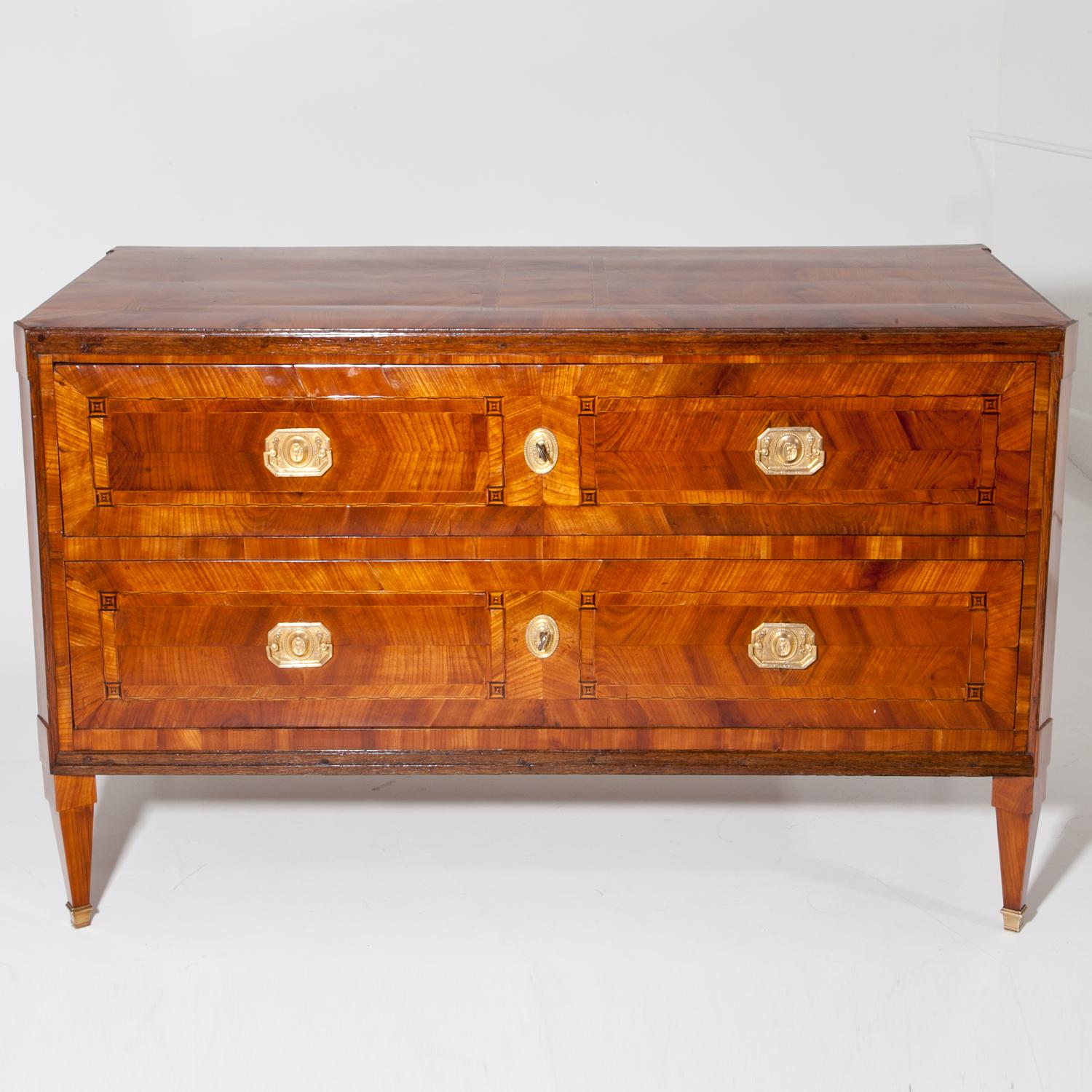 Neoclassical chest of drawers standing on angled tapered legs with brass sabots. The chest has two drawers and shows a beautiful cherrywood veneer pattern with inlays accentuating the front, top and sides. Very beautiful, hand-polished condition.