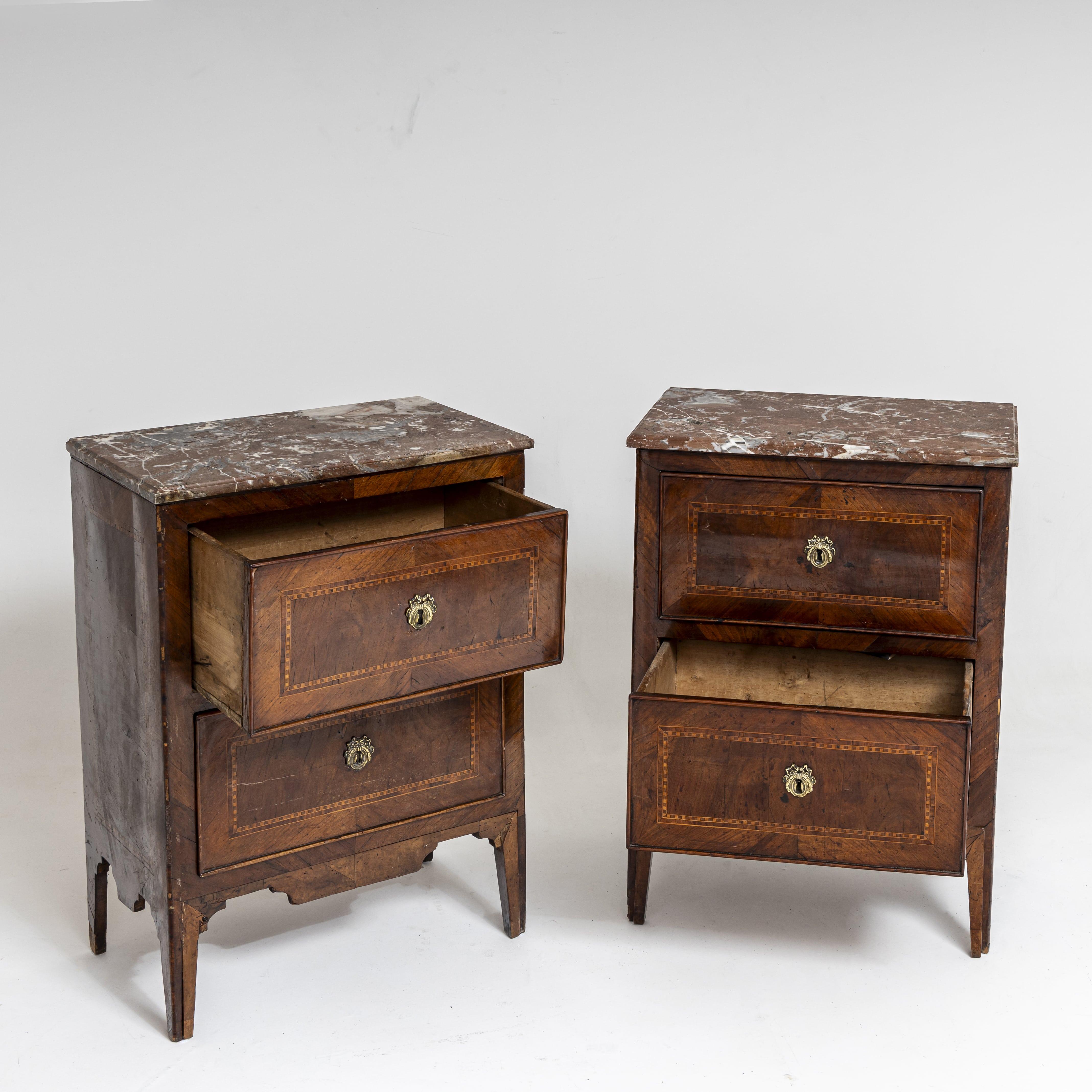 Pair of neoclassical chests of drawers featuring red and white marble tops and a body with walnut veneer and two drawers. The drawer fronts boast intricate inlays and are adorned with bronze fittings. These chests of drawers retain their original,