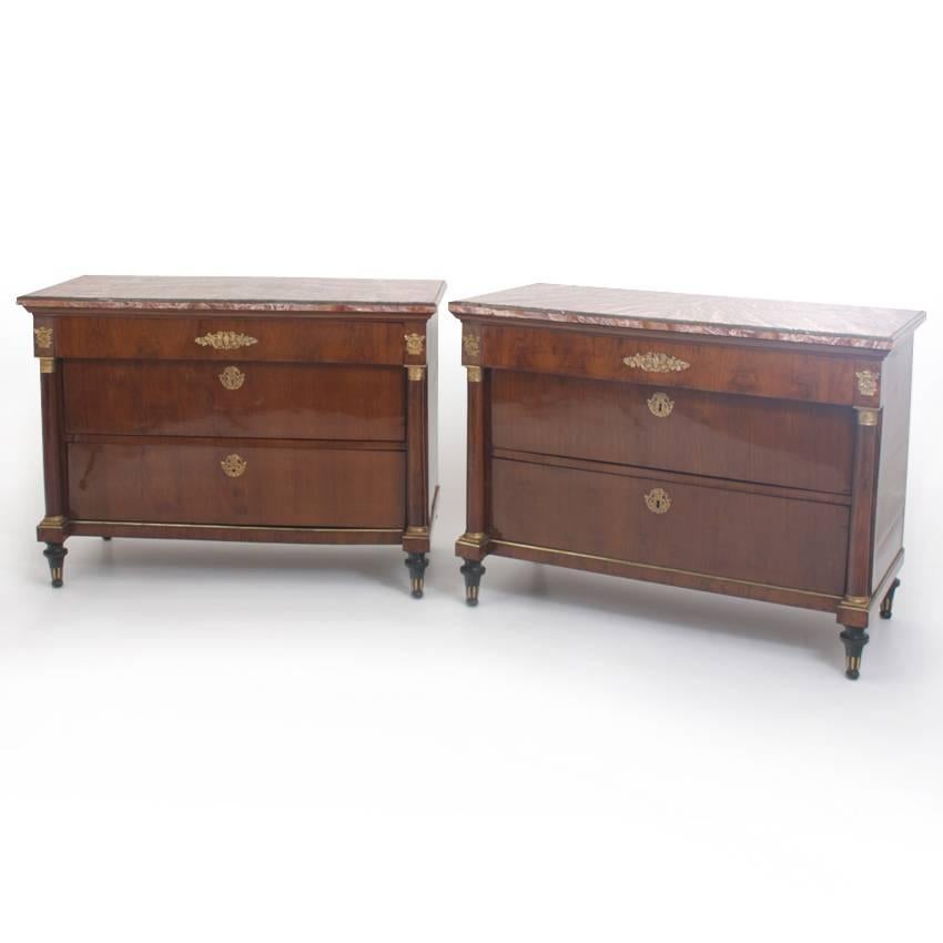 Pair of neoclassical walnut chests of drawers with fluted blackened feet and full columns with bronze capitals and bases. The chests have three drawers and are decorated with bronze fittings. The tops are red and green marble.