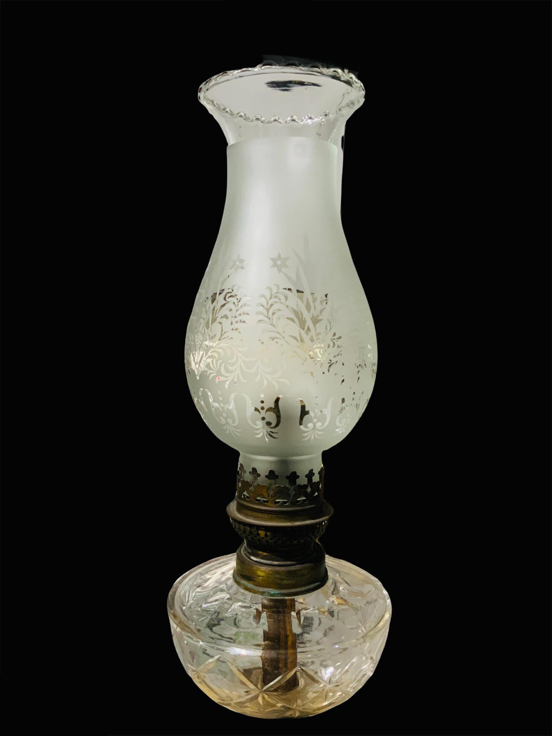 This is an elegant neoclassical column oil lamp that was electrified. The lamp consists of a tulip shaped frosted clear shade that is adorned with palmettos, foliage and stars. Below it, it is the brass burner followed by a cut crystal oil basin.