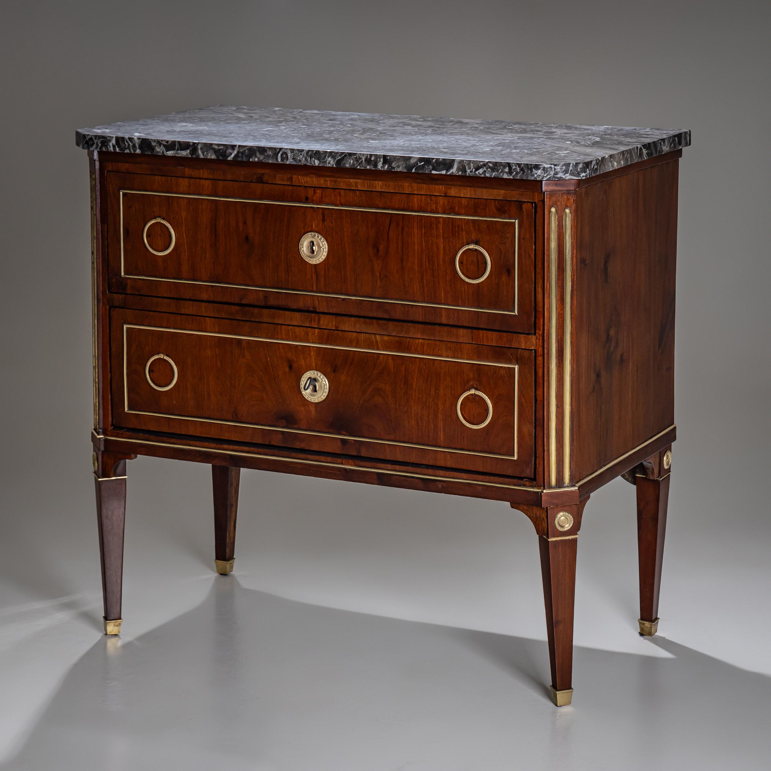 Neoclassical commode from around 1800, featuring two drawers and fine mahogany veneer. The top is made of gray marble and framed with brass trim, enhancing the refined appearance. The chamfered corners of the body are decorated with vertical