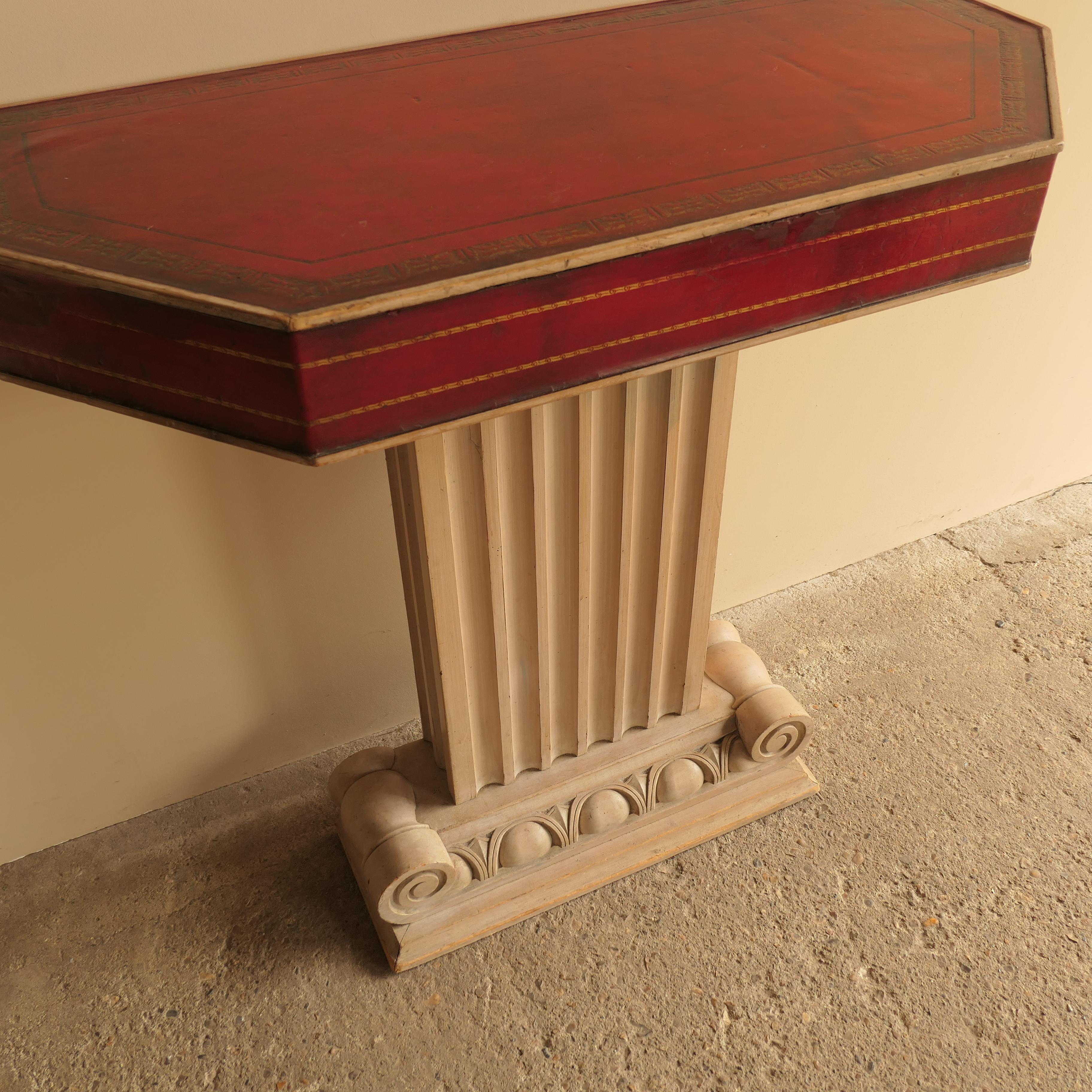 Una elegante consola de estilo neoclásico, elaborada a la manera de John Stuart. Esta pieza atemporal presenta una refinada base arquitectónica con detalles decorativos en forma de columna y una tapa de cuero ricamente texturizada. Ideal para añadir